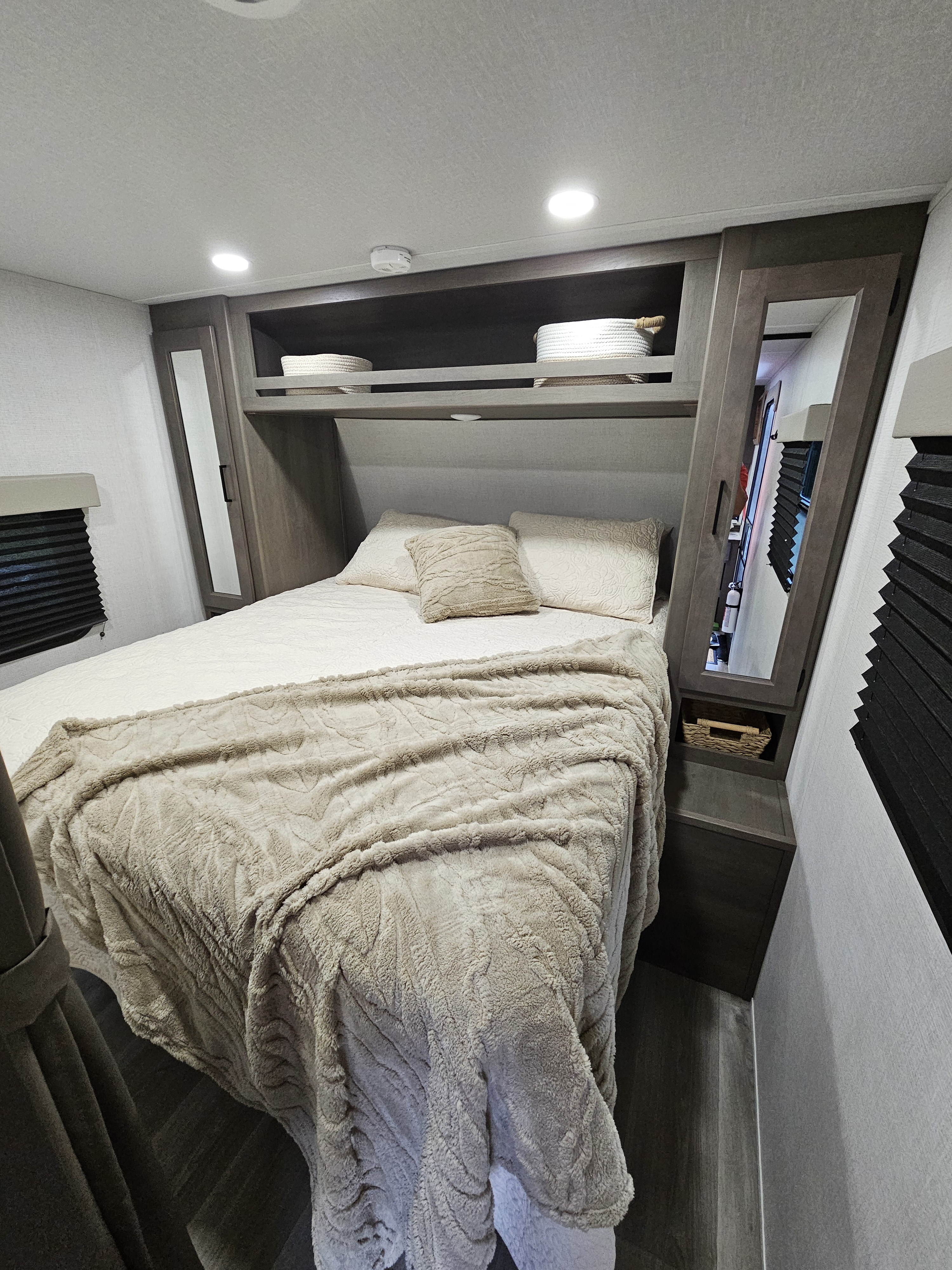 Compact RV rental bedroom featuring a comfortable bed with neutral bedding, overhead storage, and integrated mirrors.. Grand Design Other 2024