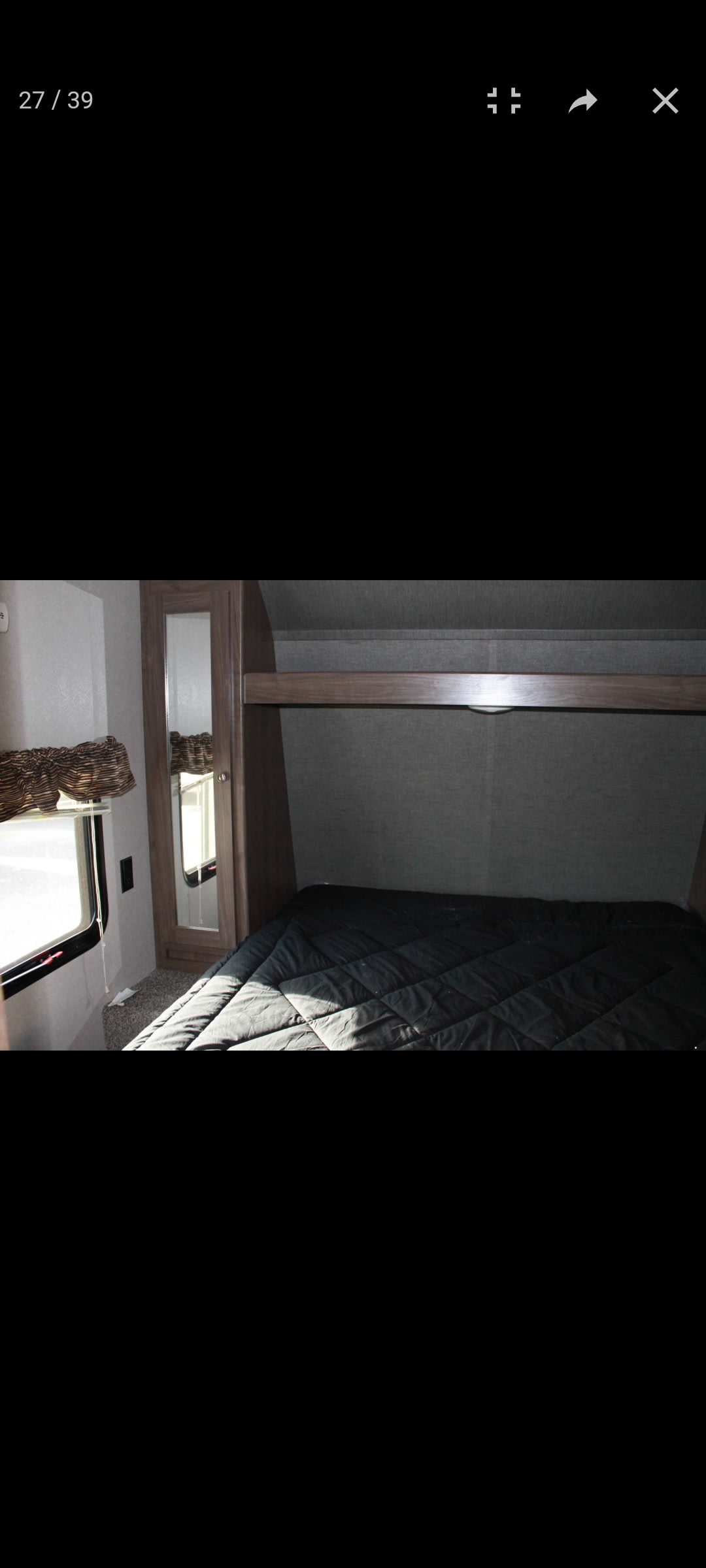 Inside an RV rental: a compact bedroom features a dark bed, window, mirrored closet, and overhead storage.. Keystone RV Hideout LHS 2018