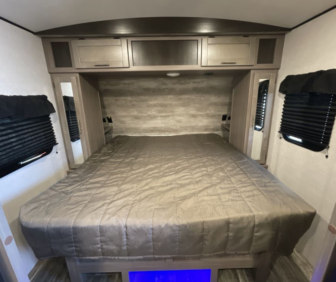 Spacious RV rental bedroom featuring a large bed, overhead cabinets, and mirrored wardrobes. Ideal for comfortable travel.. Crossroads RV Sunset Trail Super Lite 2022