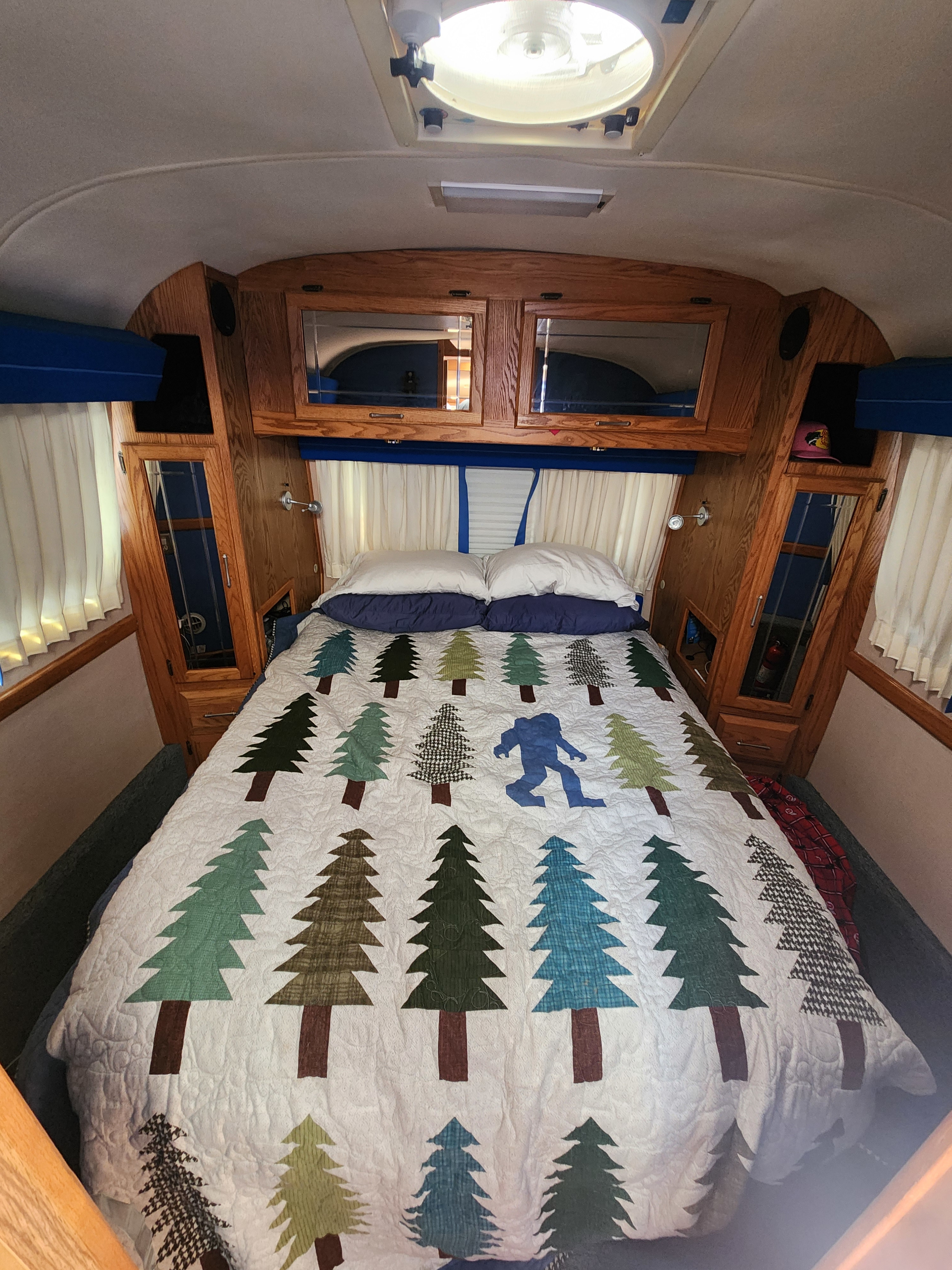Cozy RV rental bedroom with unique tree & Bigfoot quilt, wood paneling, and an overhead light fixture.. Airstream Limited 2000