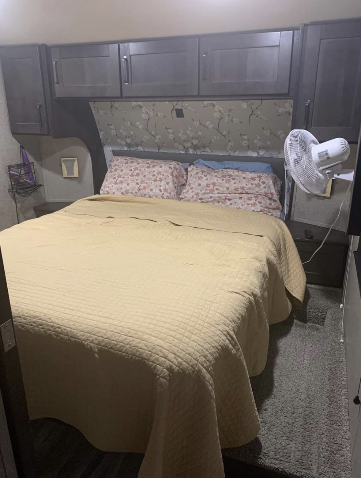 RV rental: A cozy bedroom with a quilted bed, floral headboard, overhead cabinets, and a mounted fan for comfort.. Grand Design Reflection 2021