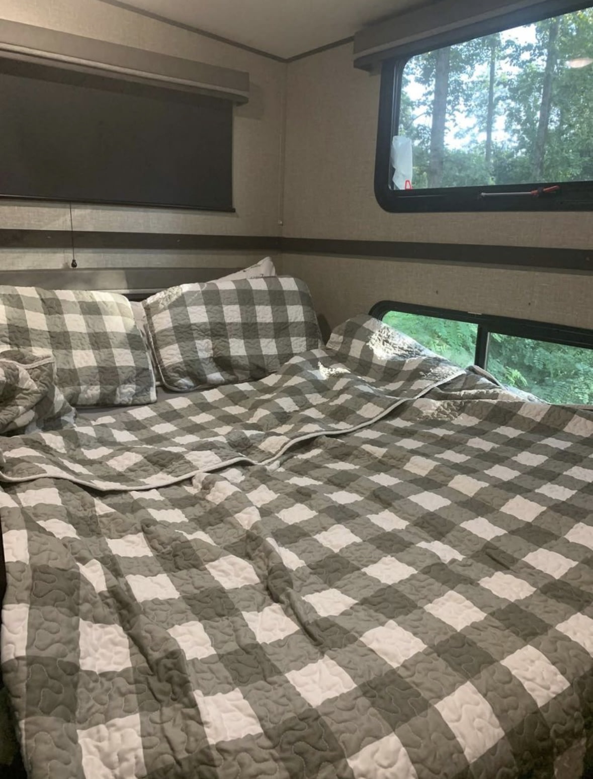 Cozy RV rental bedroom with gray and white checkered bedding and scenic window views of trees.. Grand Design Reflection 2021