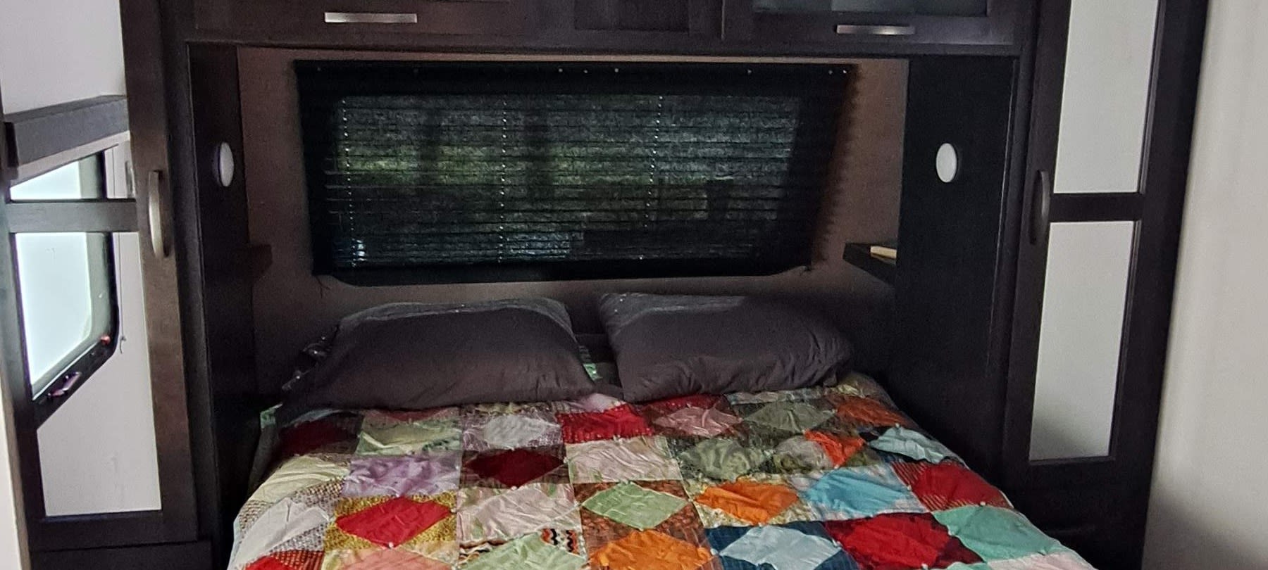 Cozy RV rental bedroom featuring a colorful patchwork quilt, overhead cabinets, and side windows.. Forest River Surveyor Luxury 2020