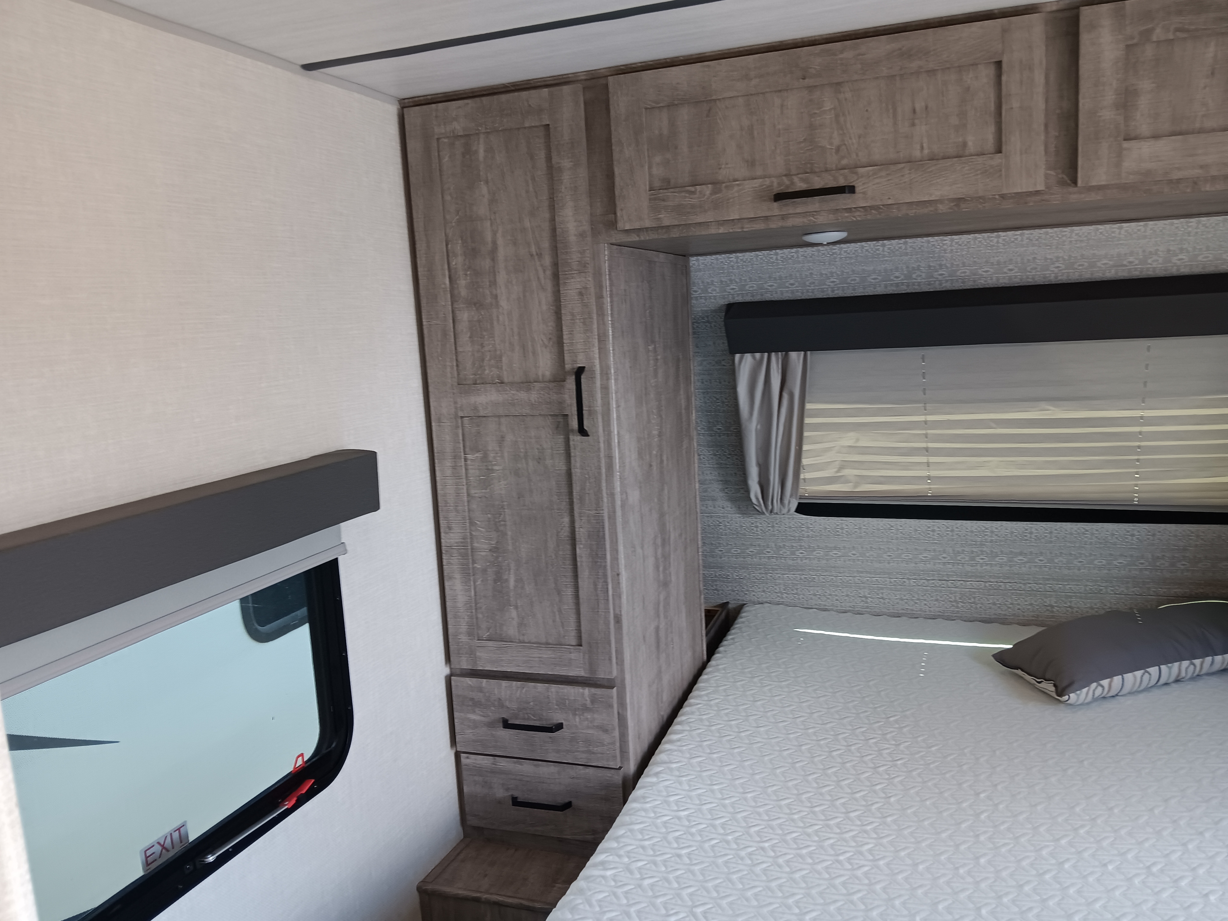 Cozy RV rental bedroom featuring a comfy bed, wardrobe, overhead storage, and windows with blinds.. Grand Surveyor 25rls 2023