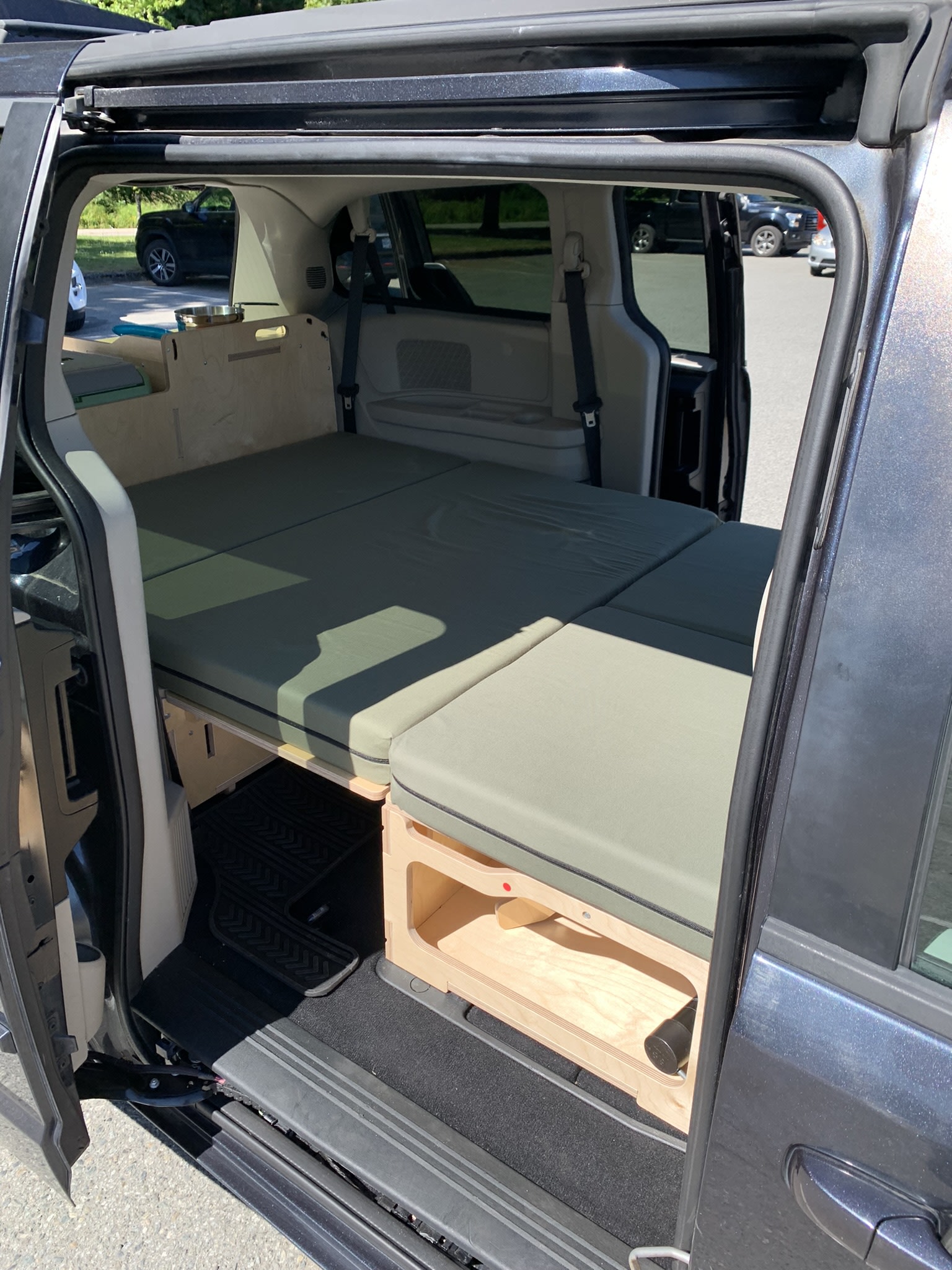 Minivan converted into a campervan with a green-cushioned bed. An ideal RV rental for flexible travel and camping.. Dodge Grand Caravan 2013