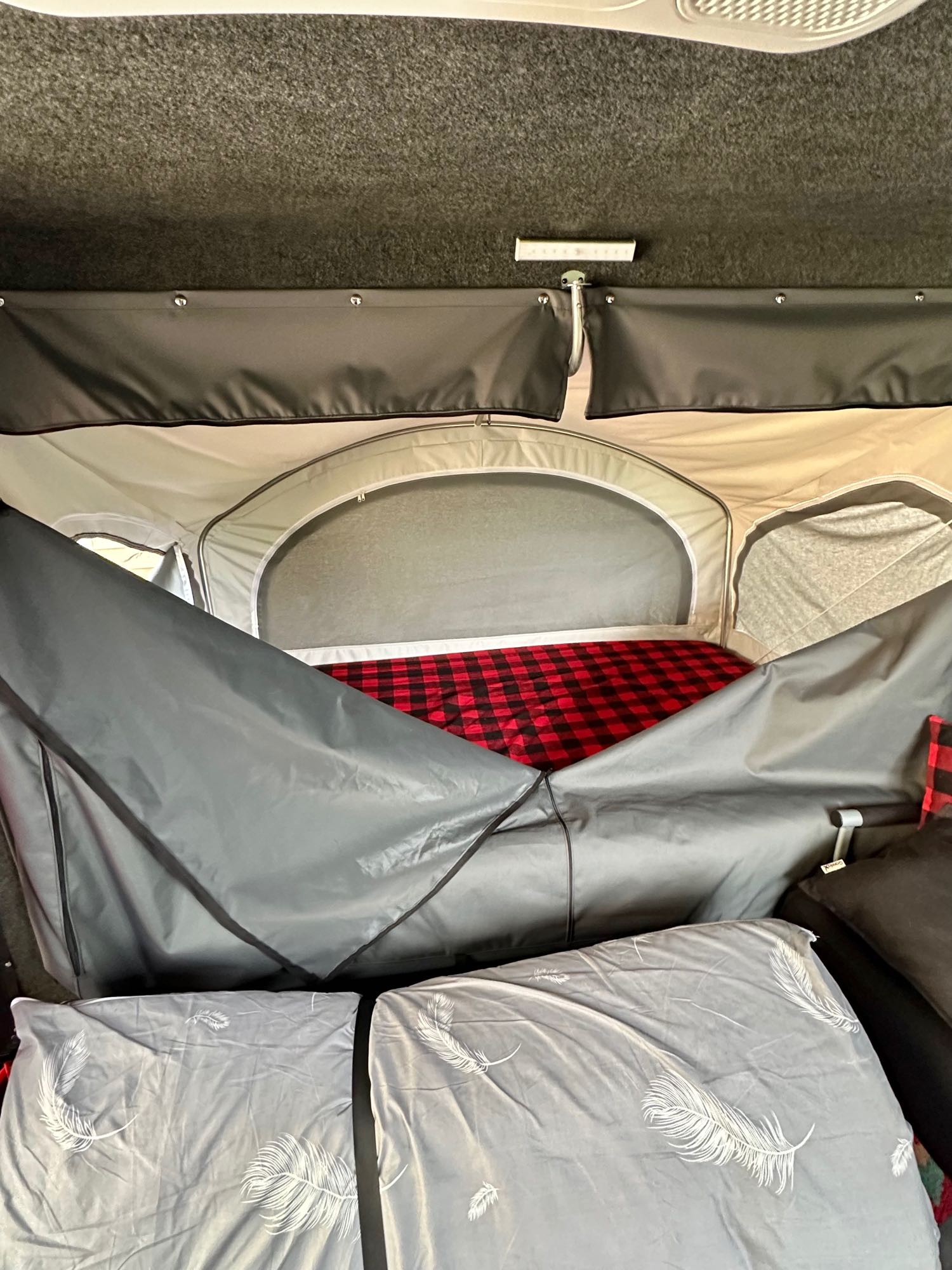 RV rental's cozy sleeping area: pop-top tent with plaid bedding & comfy pillows for adventure.. Intech Explore 2023