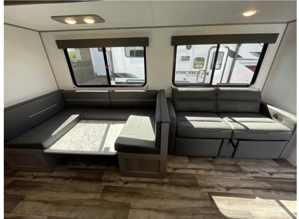 Spacious RV rental living area with a dark grey U-shaped dinette and sofa, ideal for travel comfort.. Dutchmen Coleman Lantern 2024
