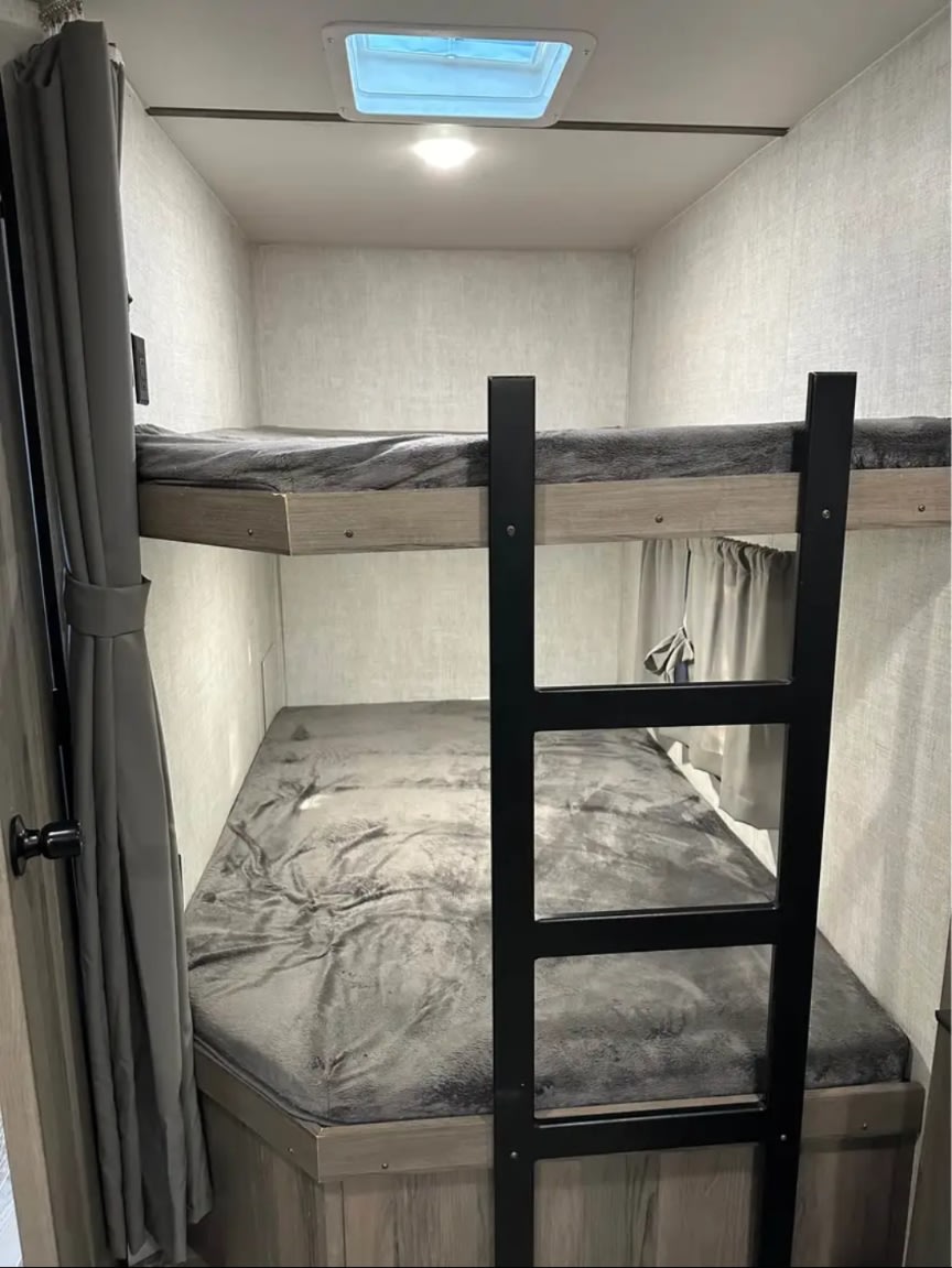 Cozy RV rental bunk beds with grey blankets and a skylight, offering compact and comfortable sleeping for your adventure.. Gulf Stream Enlighten 2021