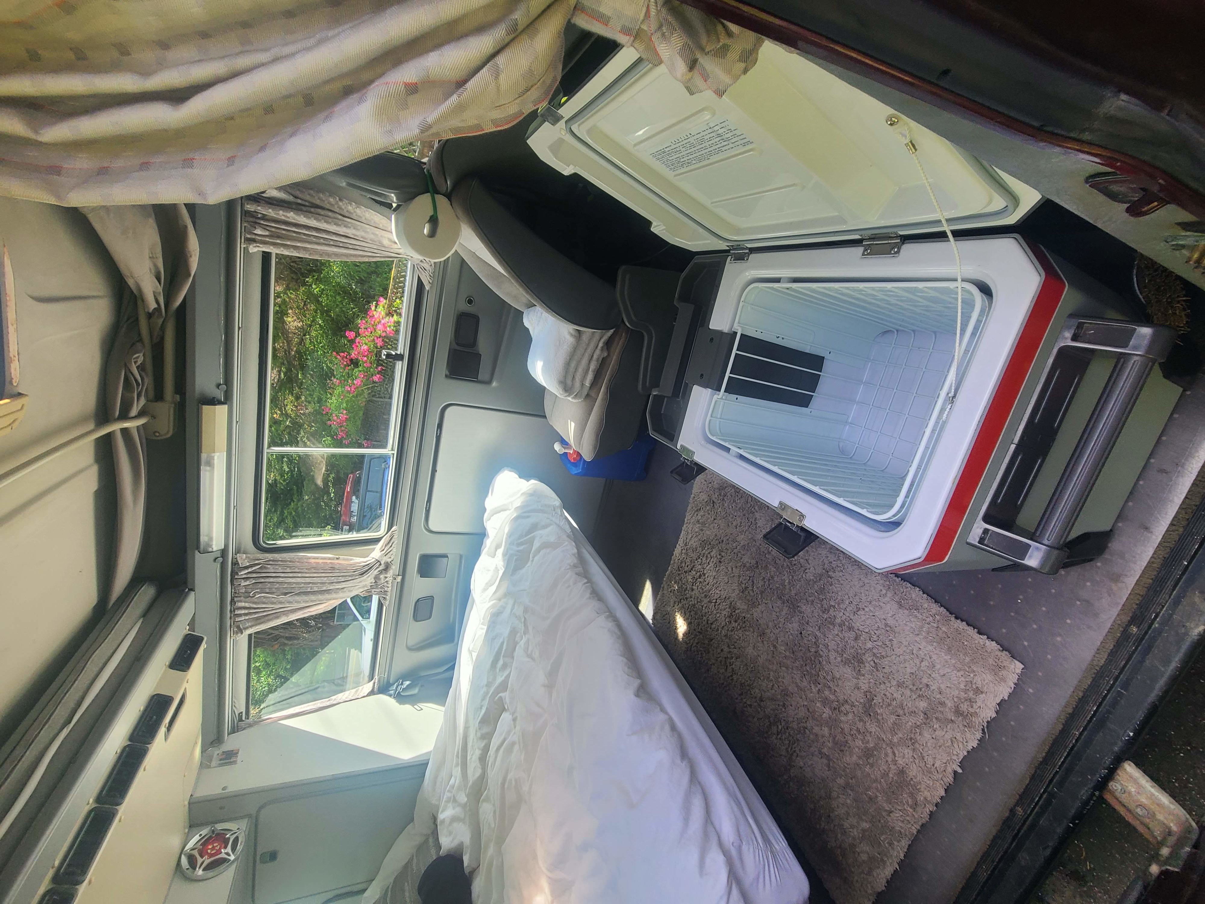 Inside an RV rental: a comfy bed, open cooler, and scenic window views for your next camping trip.. Volkswagen T3 Mulitvan 1991