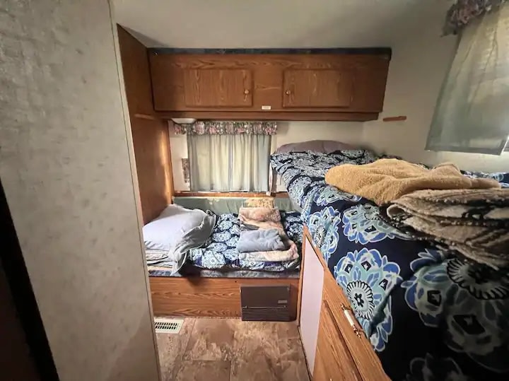 Cozy RV rental interior showing bunk beds with blue bedding, an additional bed, and overhead cabinets for a comfortable stay.. Heartland Mallard 1995