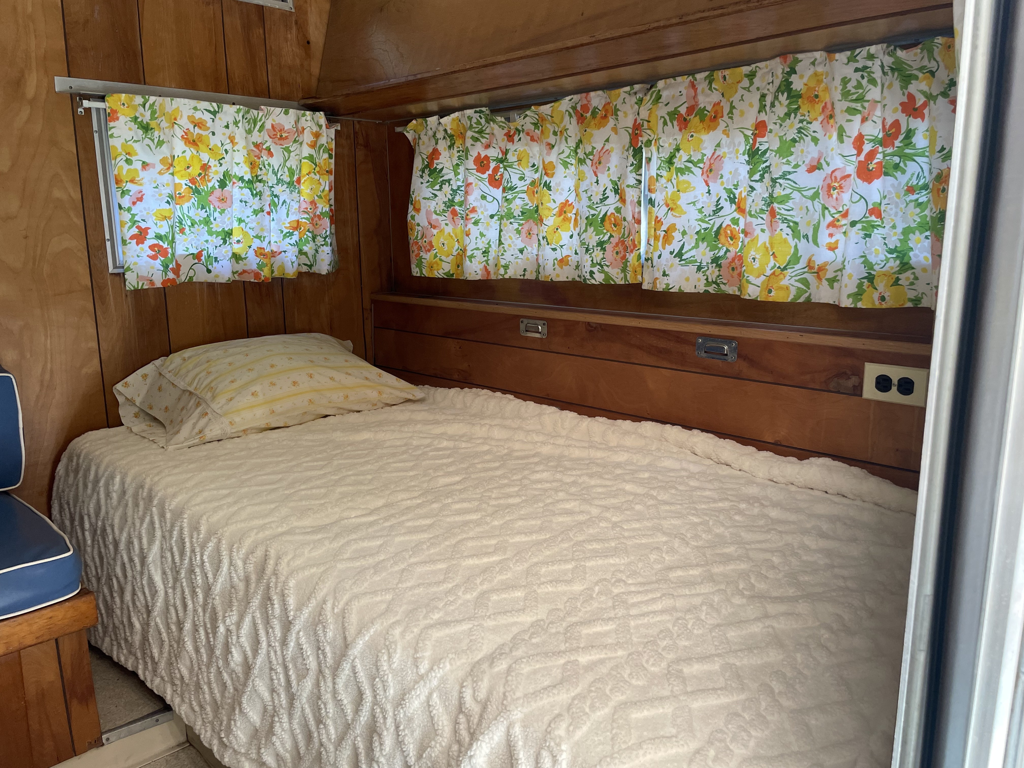 Cozy RV rental bedroom: bed with a textured white blanket, yellow pillow, wood walls, and vibrant floral curtains.. Forest River Forester 1967
