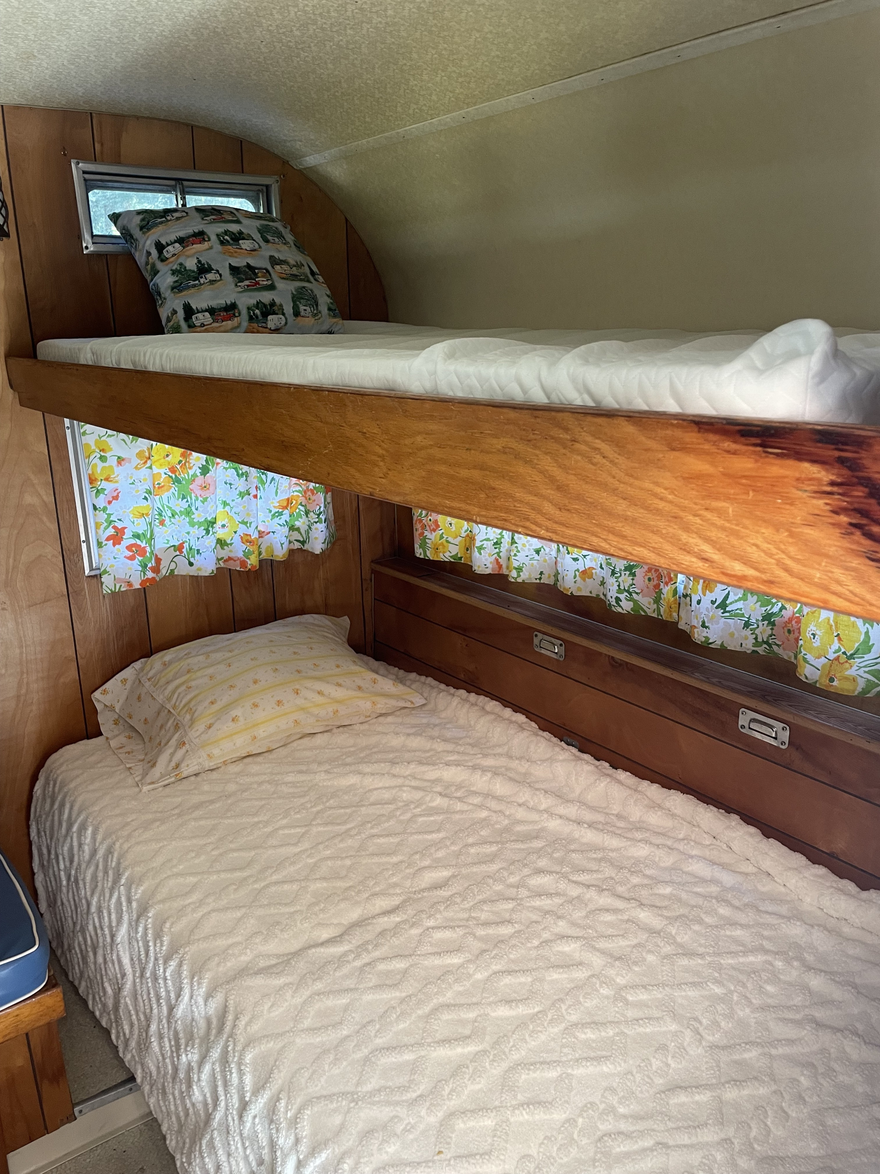 Inside an RV rental: cozy bunk beds with a camper-patterned pillow on top & white blanket on bottom. Floral curtains & wood.. Forest River Forester 1967