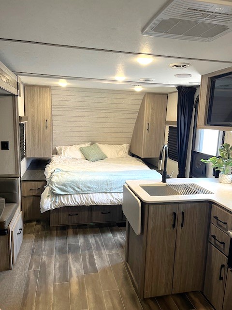 Cozy RV rental features a modern bedroom, compact kitchen, and stylish wood-look floors. Perfect for your next adventure.. Keystone Passport Sl series 2021