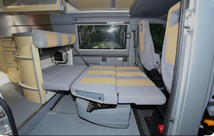 This RV rental interior features a grey/beige modular seating system that converts to a bed, with side storage cabinets. Ideal for camper van travel.. Mercedes-Benz Sprinter 2005