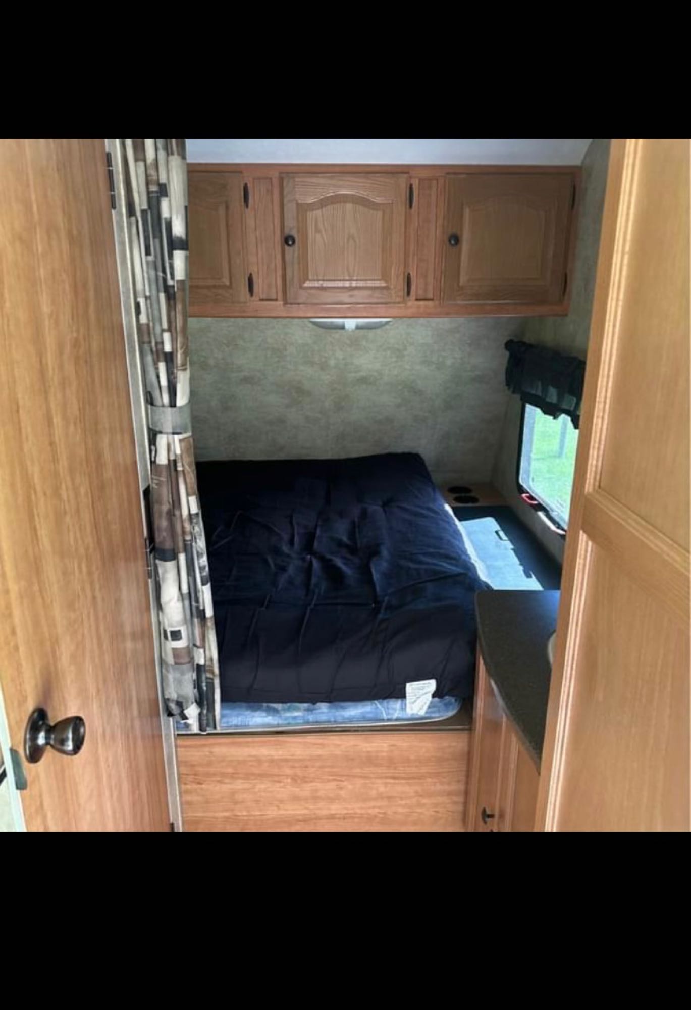 Compact RV rental interior with bed, overhead storage cabinets, and a window.. Keystone Passport 2009