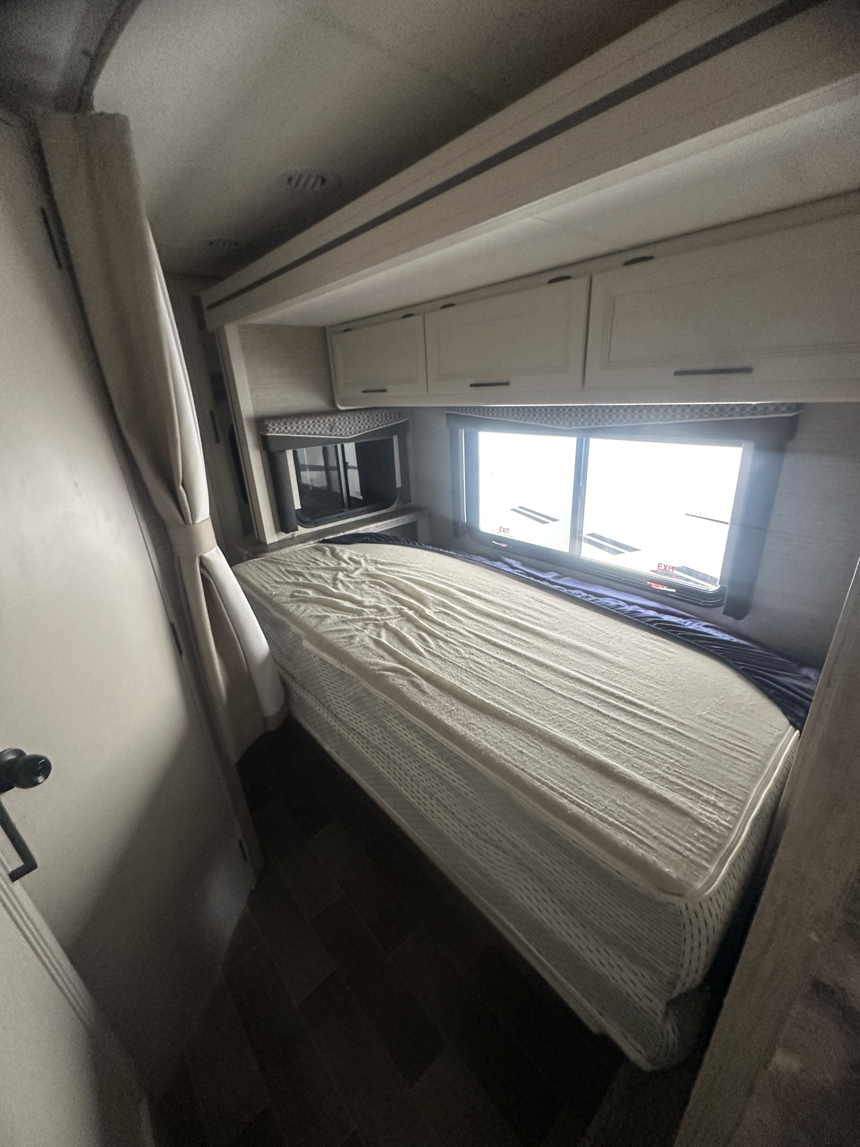 RV rental interior: A cozy bedroom with a bed, overhead cabinets, and bright windows, including an exit window.. Thor Motor Coach Chateau 2022