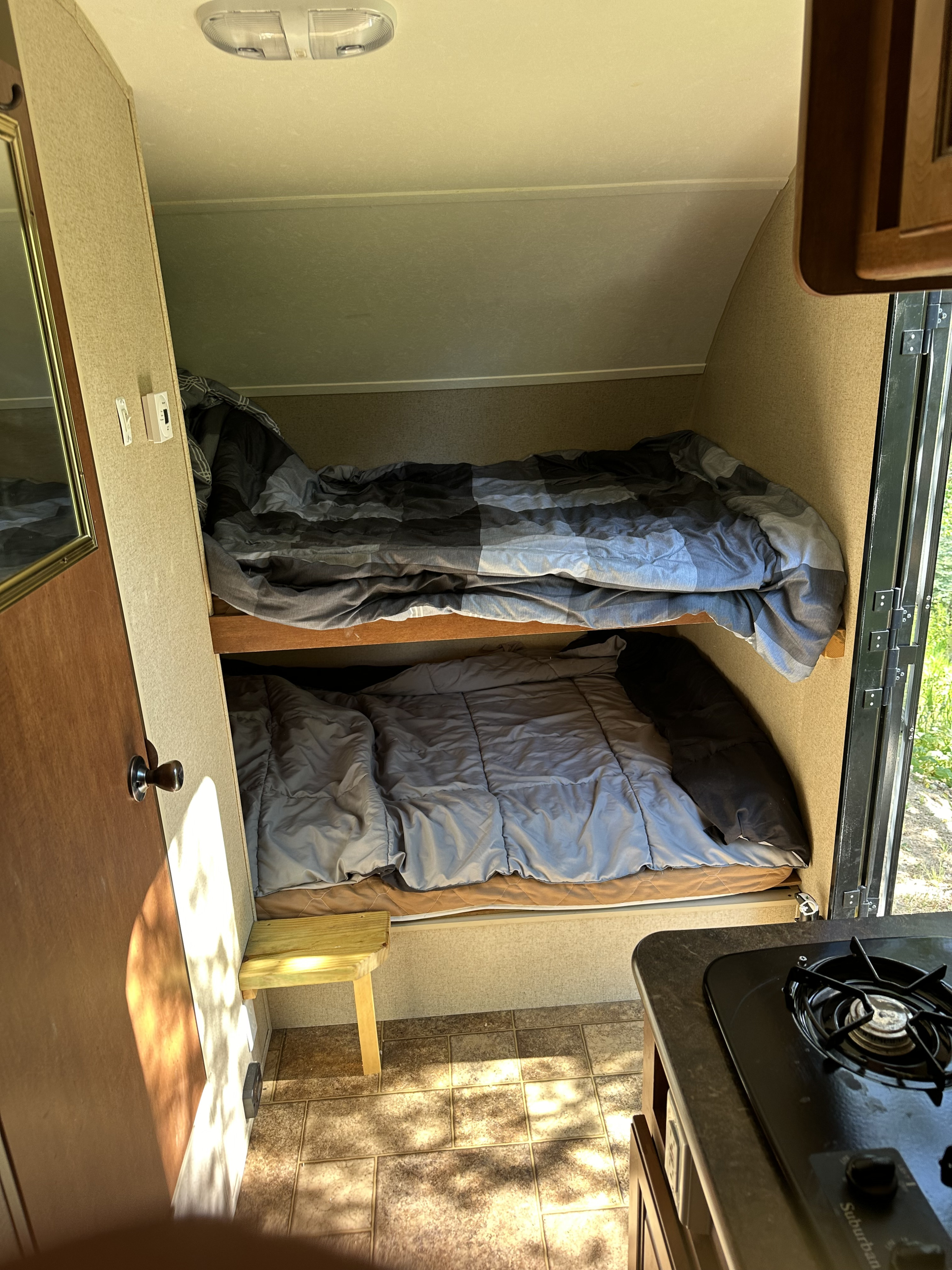 An RV rental's cozy interior, showcasing bunk beds with bedding, a compact kitchen with a stove, and tiled flooring.. Forest River R-Pod 172 2014