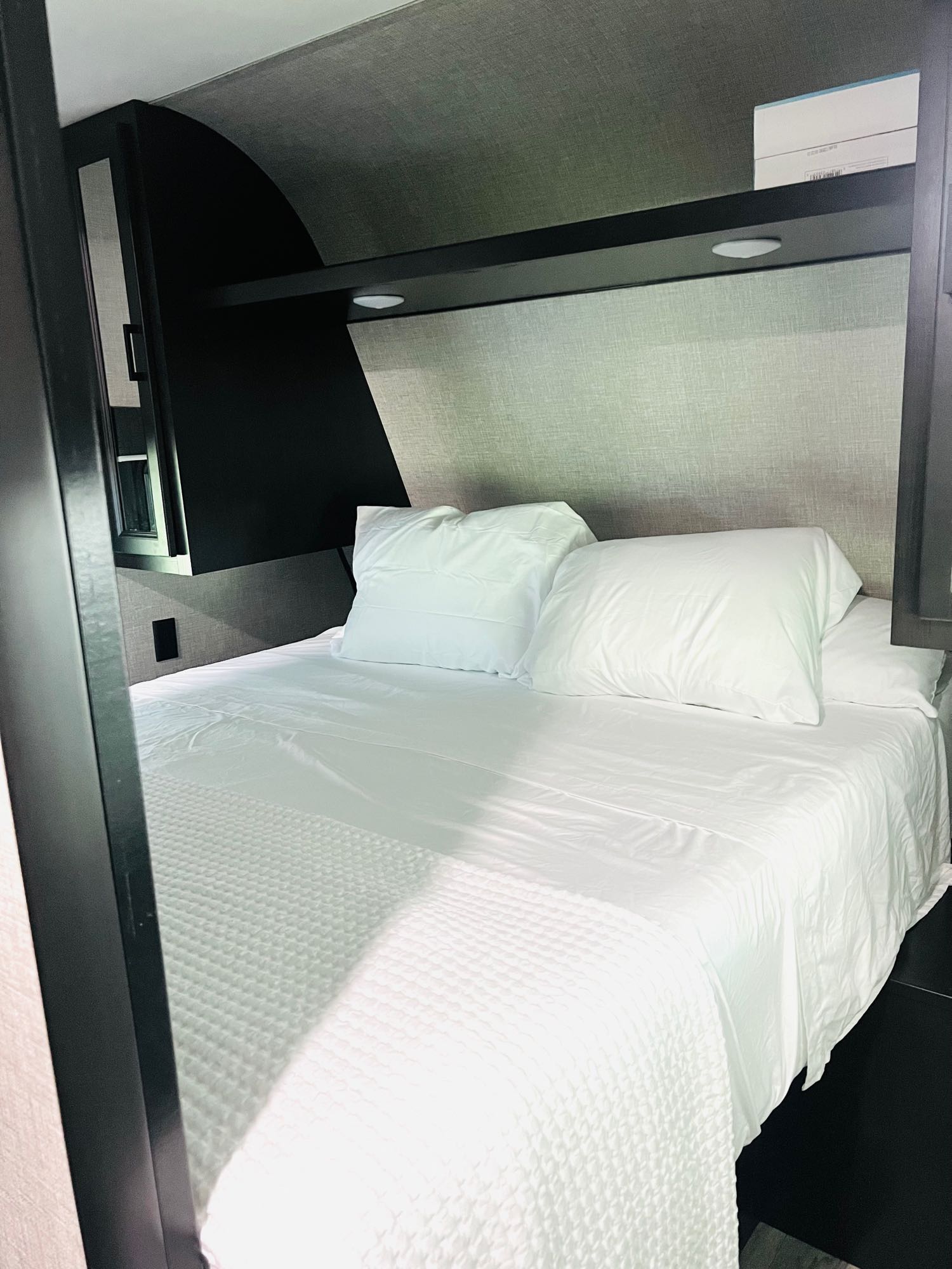 A neatly made bed in an RV rental, featuring crisp white sheets, pillows, and integrated overhead storage.. Jayco Jay Flight SLX 2022