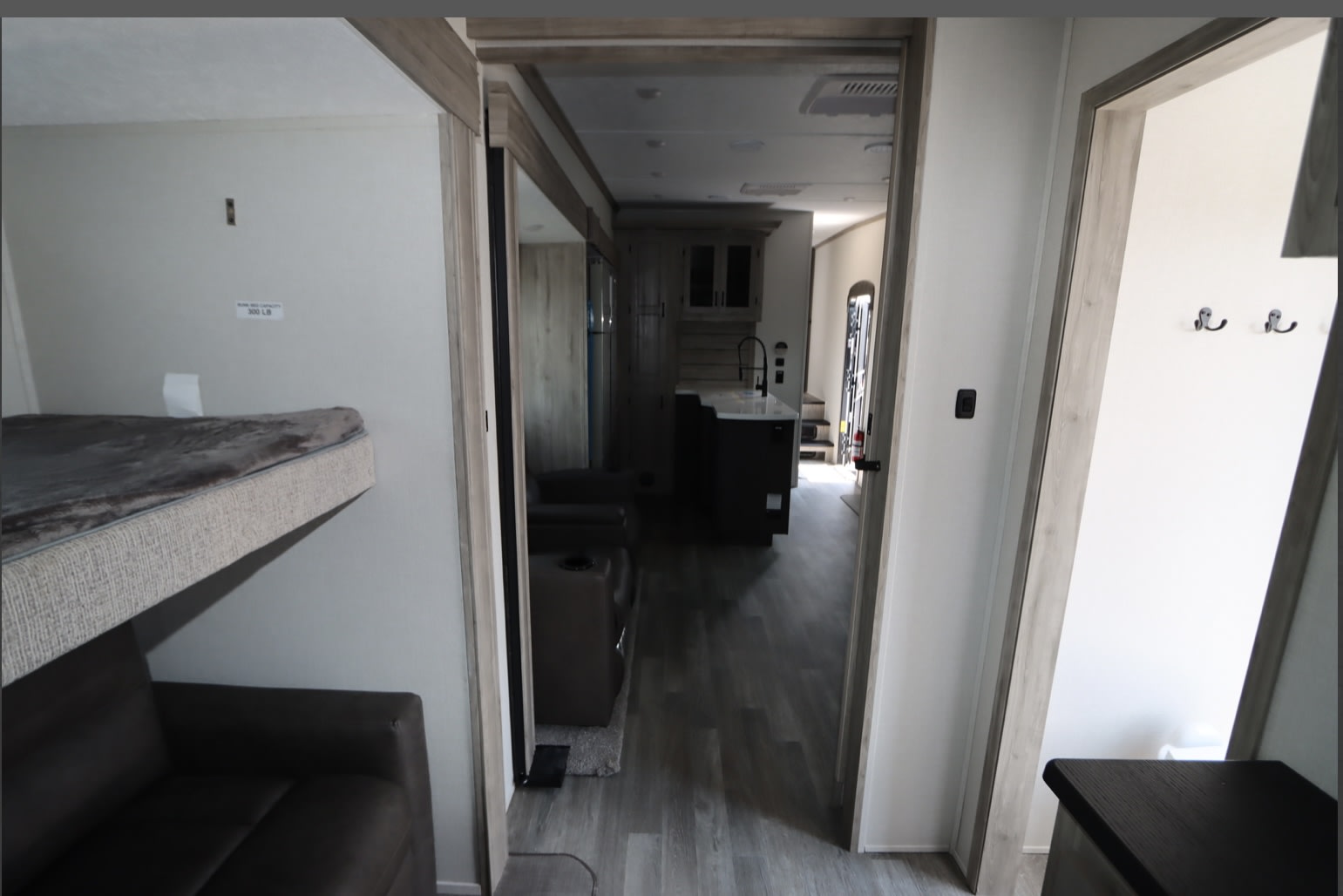 Modern RV rental interior: Bunk beds over a sofa, leading to a functional kitchen & living area. Hooks visible on the right.. Coachmen Chaparral 2024