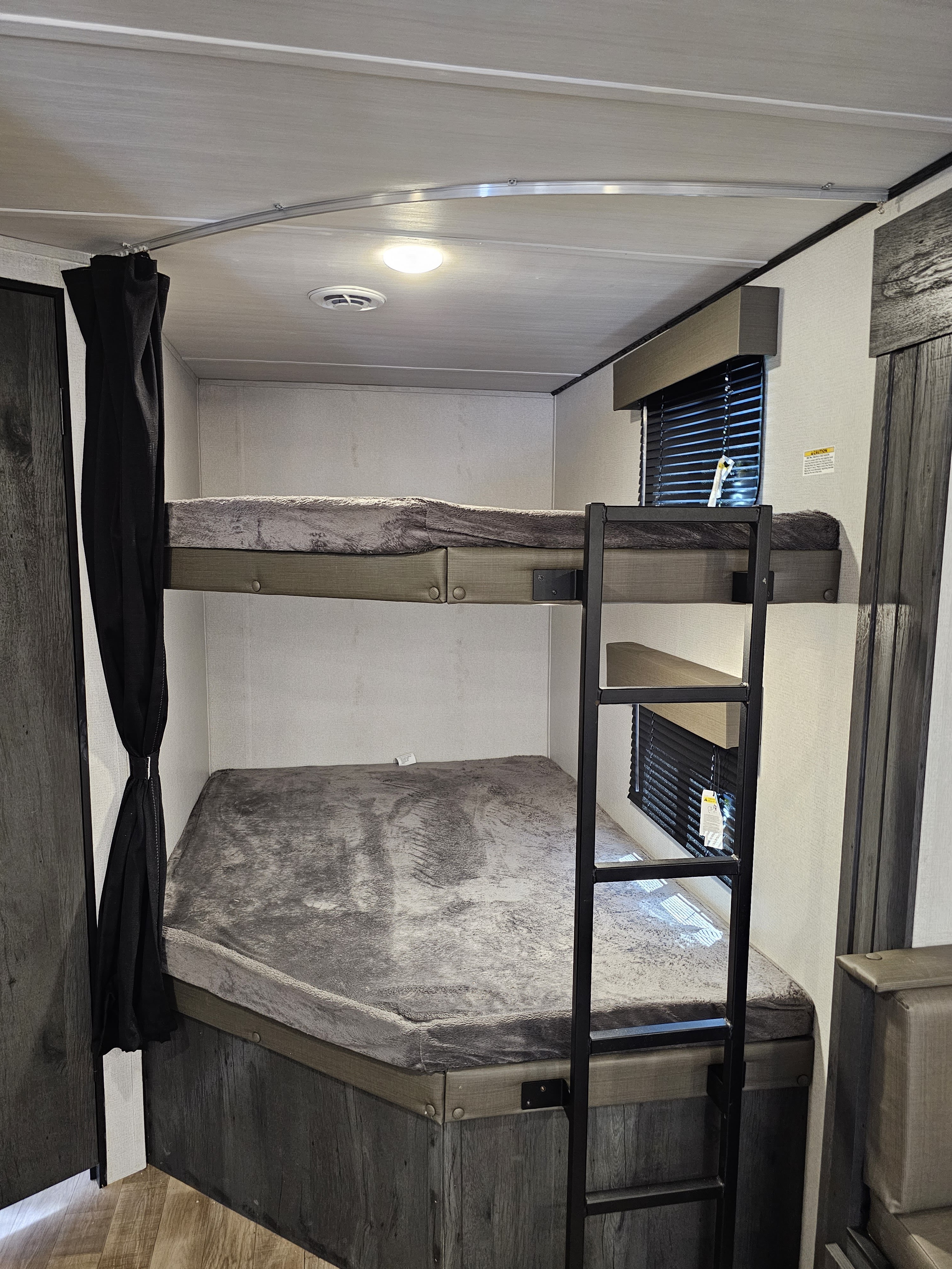 Cozy bunk beds in an rv rental, featuring soft gray bedding, a privacy curtain, and a ladder for the top bunk.. Keystone RV Hideout 2023