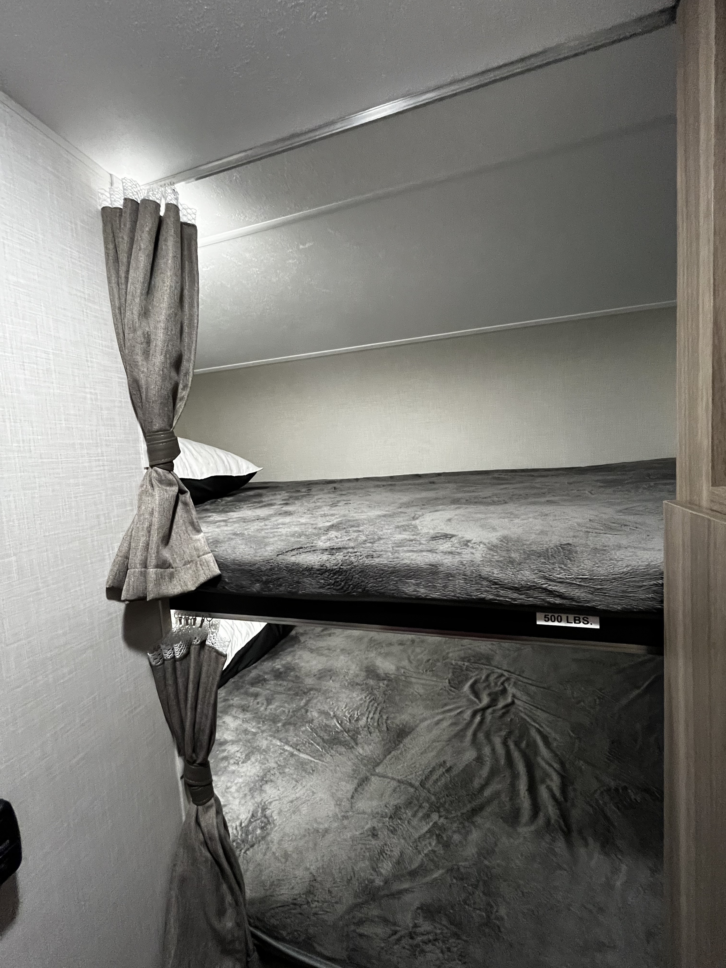 Cozy bunk beds in an RV rental, featuring grey bedding. The top bunk clearly shows a 500 LBS weight limit.. Venture SN211VDB 2024