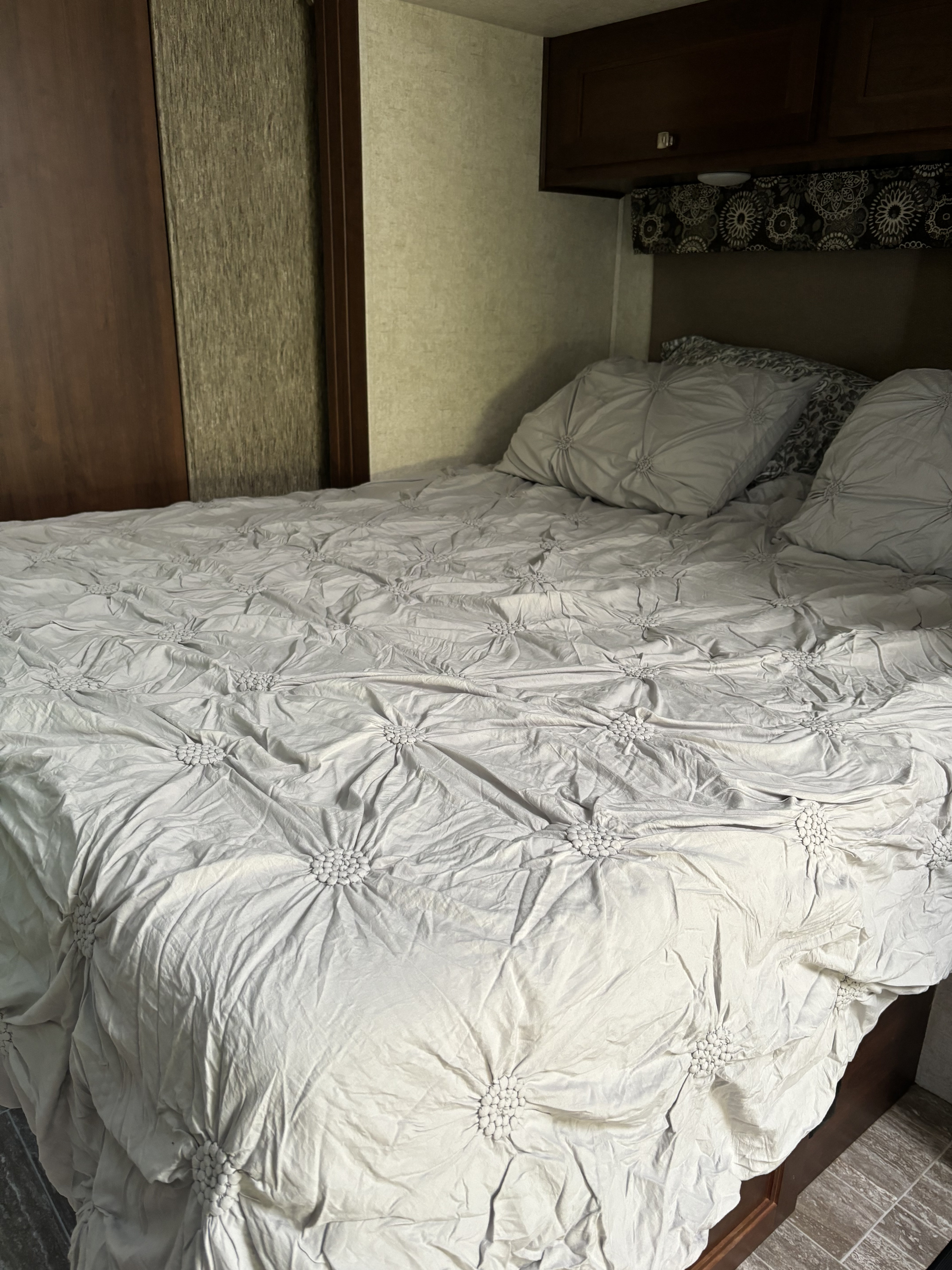 Cozy RV rental bedroom featuring a bed with textured grey bedding and pillows, overhead cabinets, and a patterned valance.. Forest River Sunseeker 2018