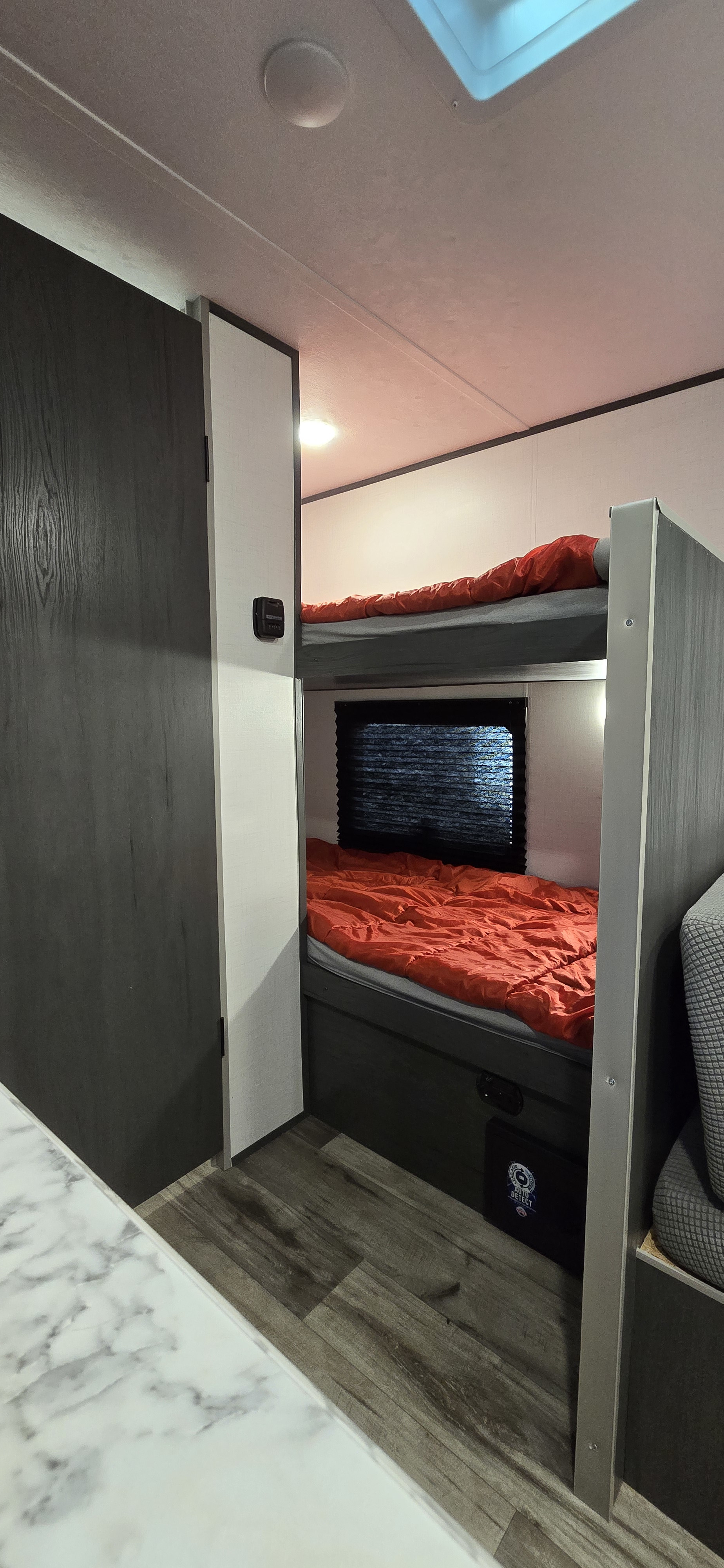 Inside a modern RV rental: cozy bunk beds with bright orange sleeping bags, wood floors, and ceiling lights.. Aspen Trail LE 2023