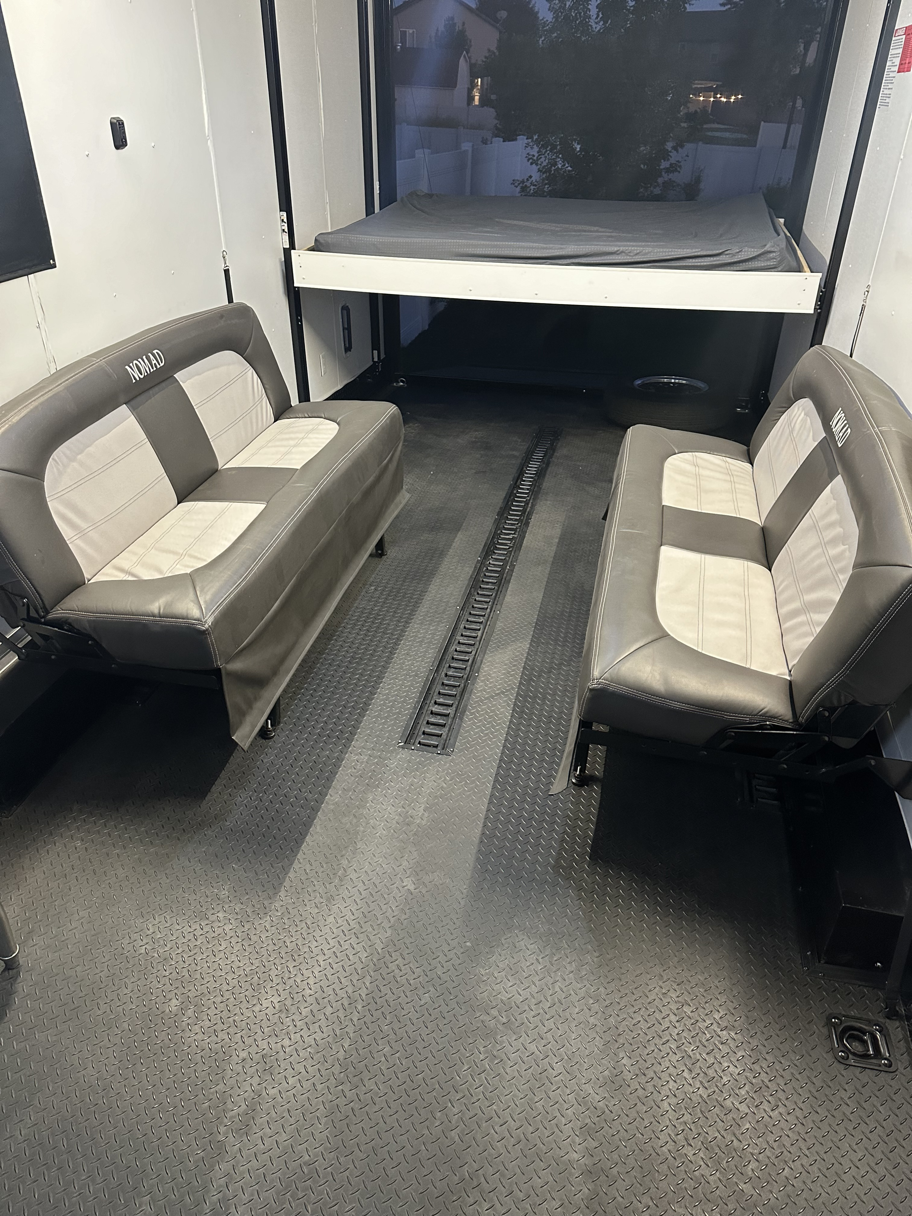 Inside an RV rental toy hauler, featuring two convertible benches, a raised bed, and durable diamond plate flooring.. Stealth Nomad 28FK 2022