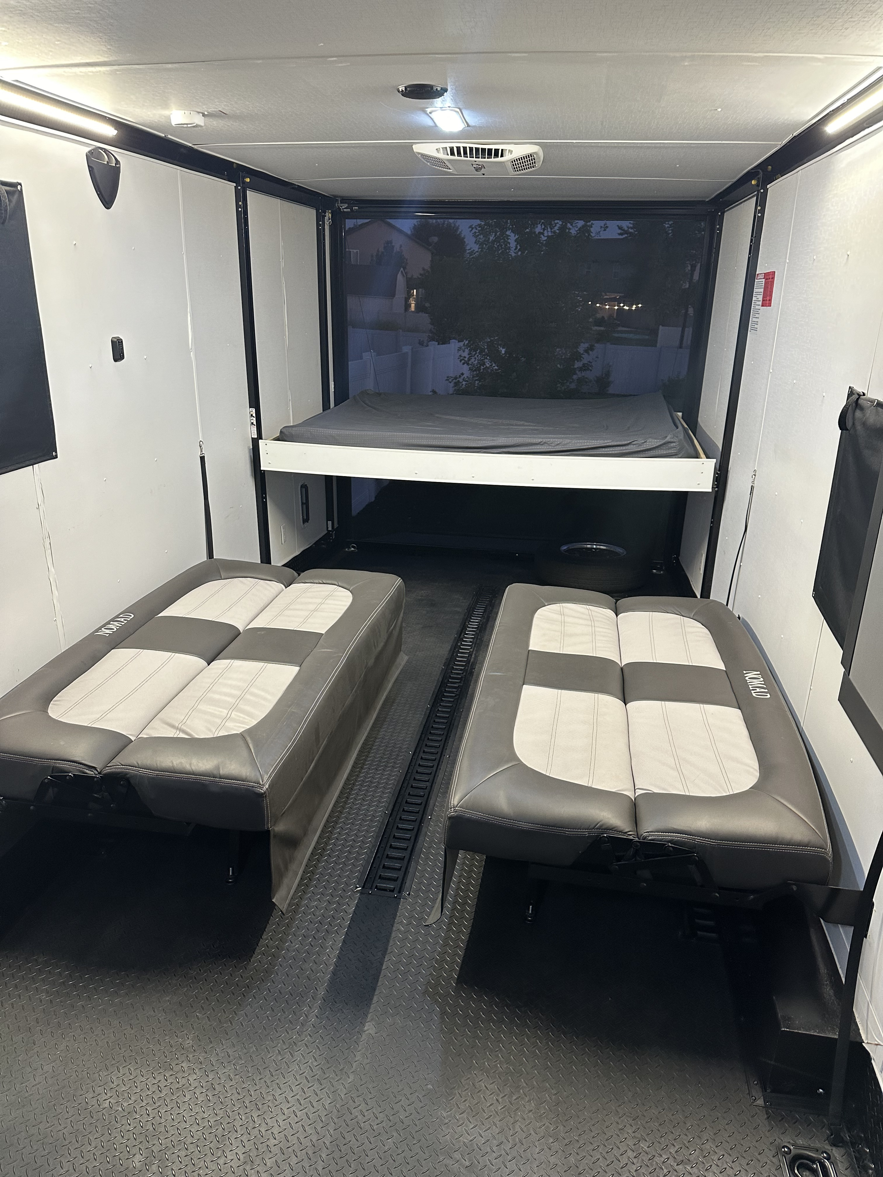 Spacious RV rental interior featuring an elevated bed, two convertible floor seats, and durable diamond-plate flooring.. Stealth Nomad 28FK 2022