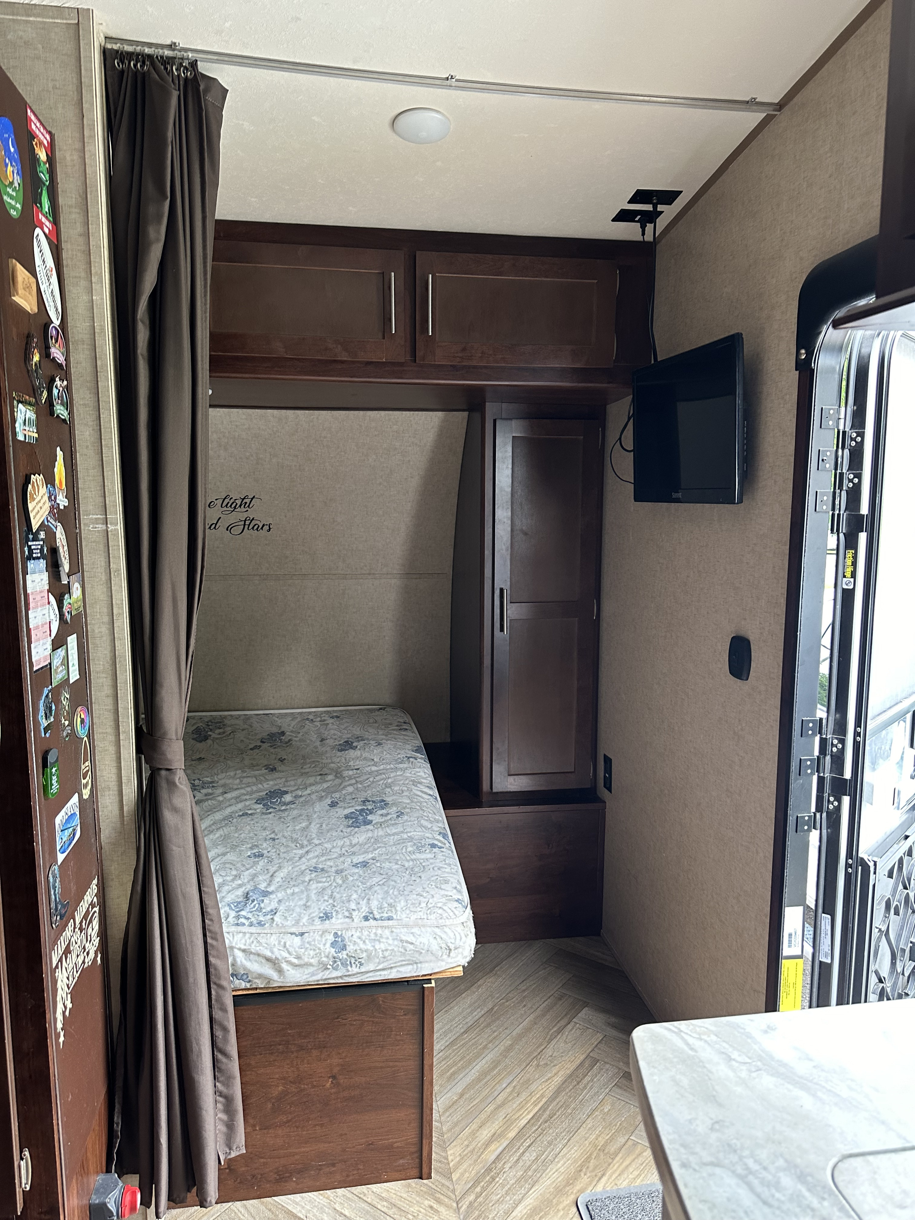 An RV rental interior featuring a compact bedroom with bed, overhead cabinets, TV, and herringbone wood floor.. Forest River Vengeance Toy Hauler 2017