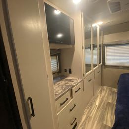 RV rental bedroom: a bright space featuring a mounted TV, modern built-in storage, mirrored closets, and dresser.. Thor A.C.E. 2021