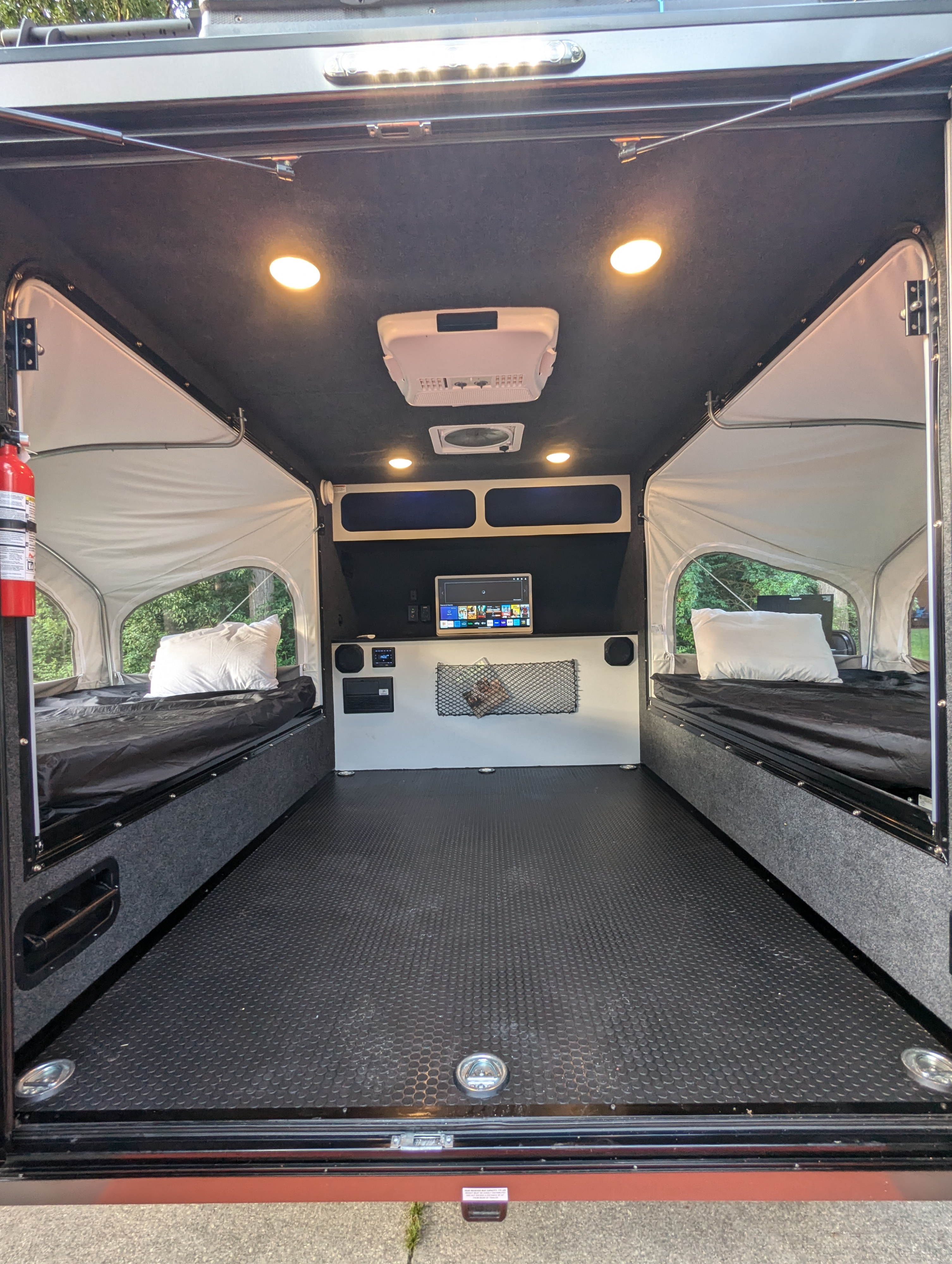 Interior of an RV rental, showing two beds with white pillows, a central floor, and a rear wall with a TV & speakers.. Intech Flyer Explore 2022