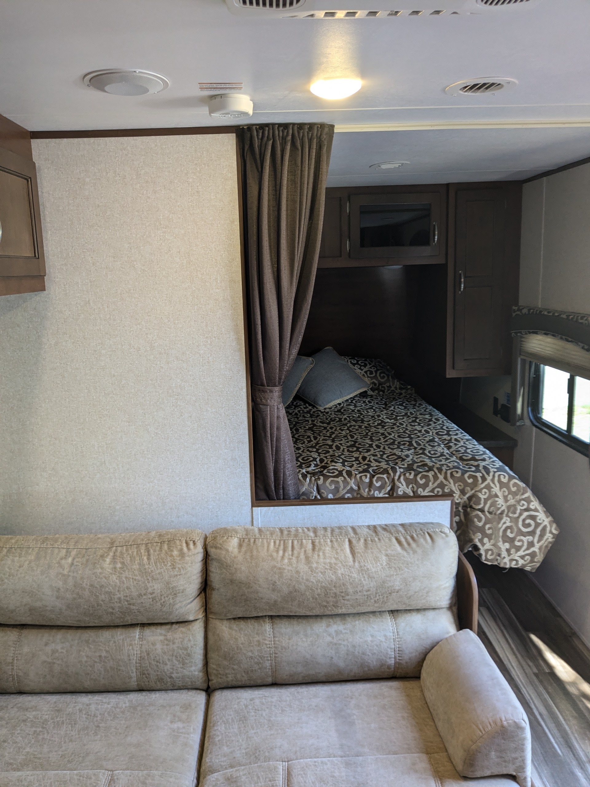 Cozy RV rental interior showing a sofa in the living area and a compact bedroom with a patterned bed beyond a curtain.. Jayco Jay Flight 2017