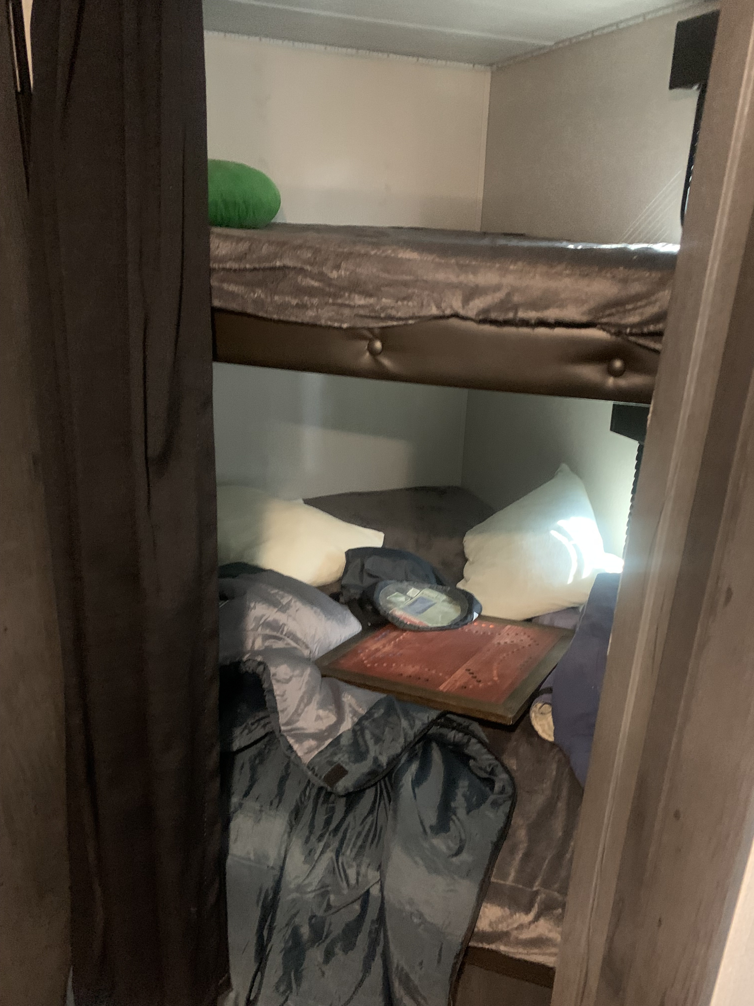 Cozy RV rental interior: bunk beds with a green pillow on top, and bedding with a board game on the lower bunk.. Keystone RV Hideout 2023