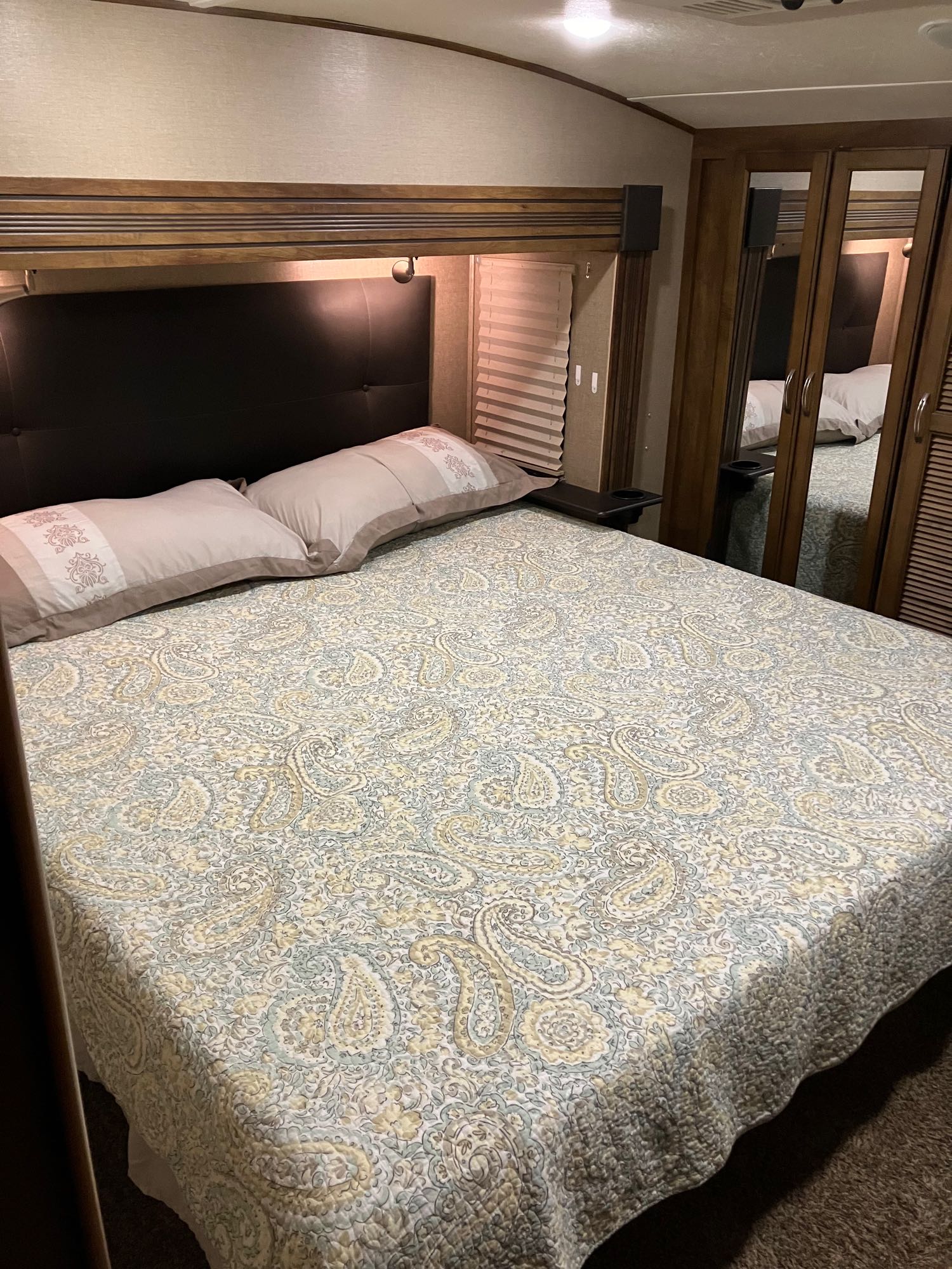 Comfortable RV rental bedroom with a queen bed, paisley quilt, built-in reading lights, and mirrored closet doors.. Forest River Coachmen Chaparral 2017