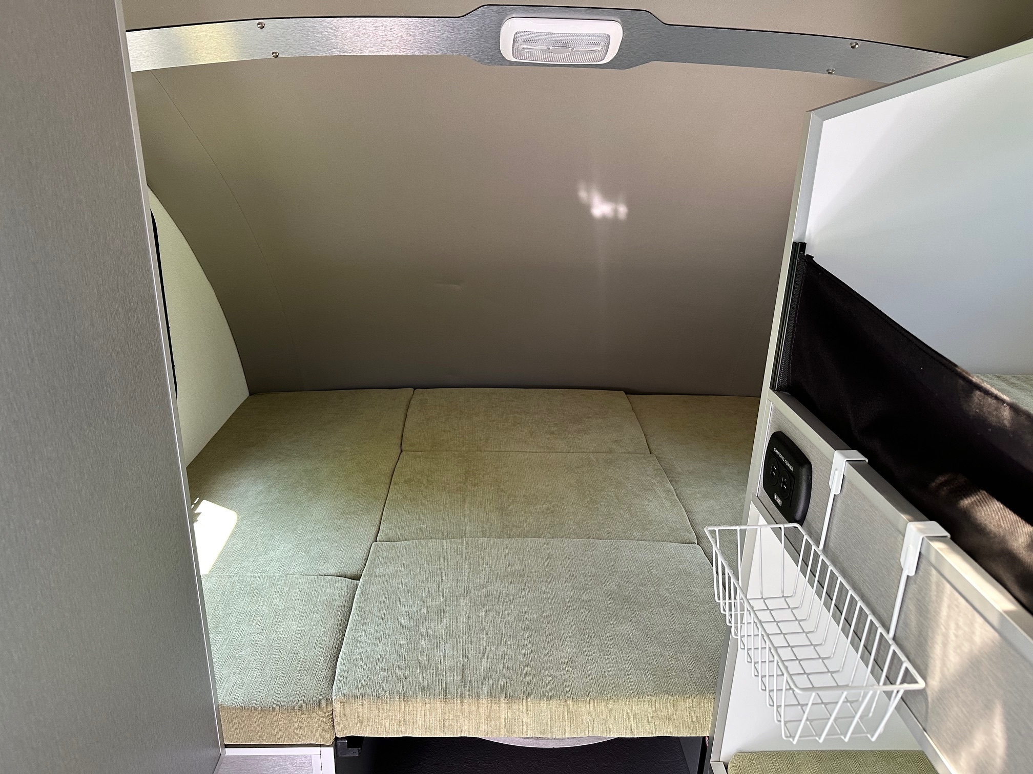 Compact RV rental interior: light green fold-out bed, overhead light, and side storage basket.. Helio O4 Evo 2023