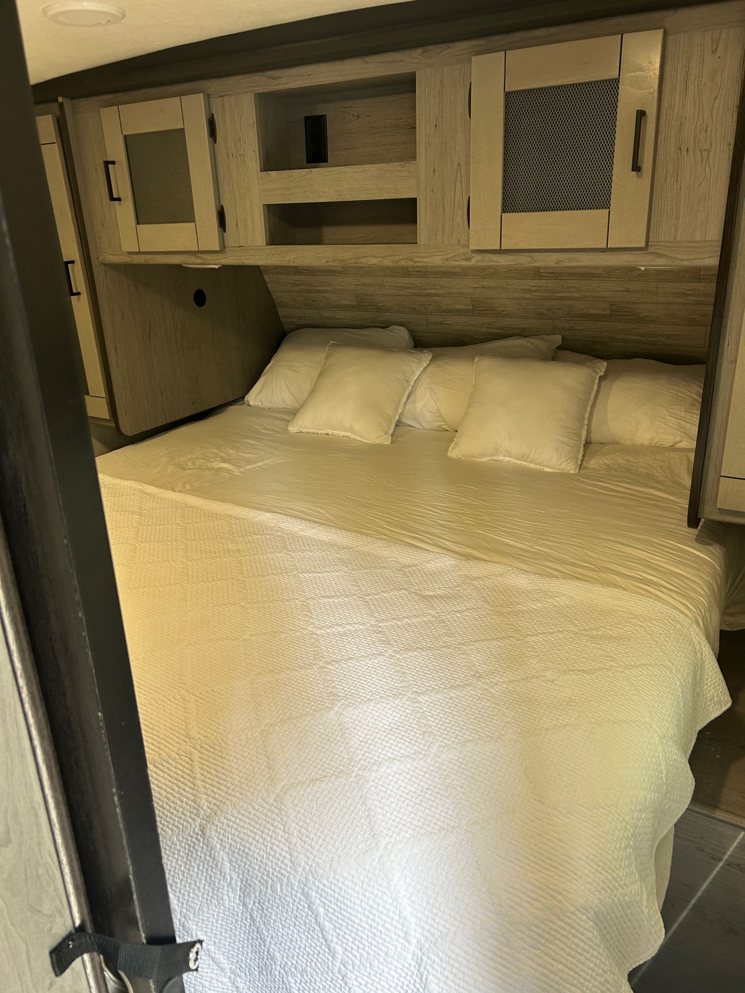 Inside an RV rental: a bright, comfortable bedroom featuring a queen bed with white linens and wooden storage cabinets.. Heartland RVs Mallard 2020