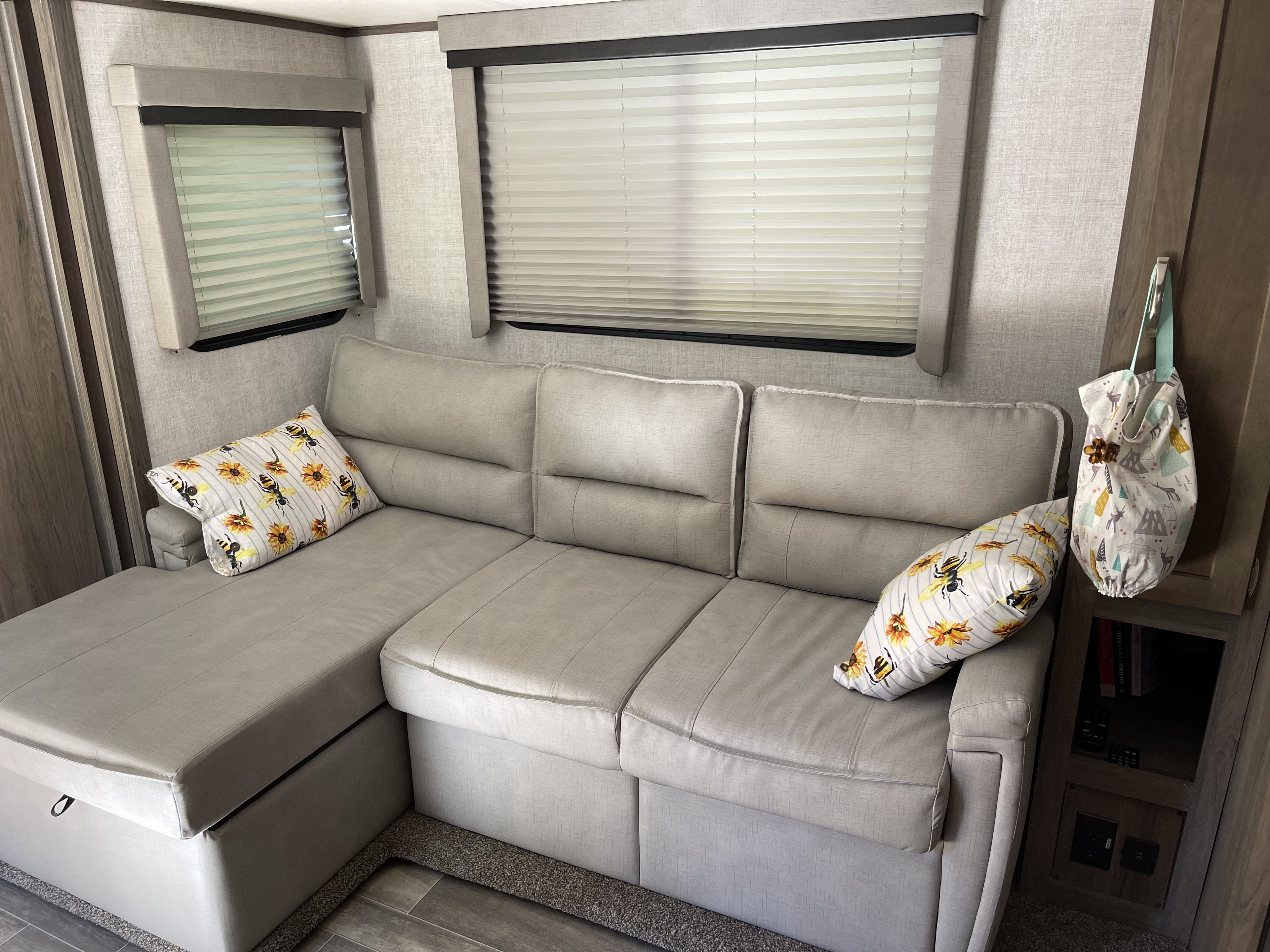 Cozy RV rental interior with a light grey sectional sofa, decorative pillows, windows with blinds, and built-in storage.. Gulf Stream Envision 2021