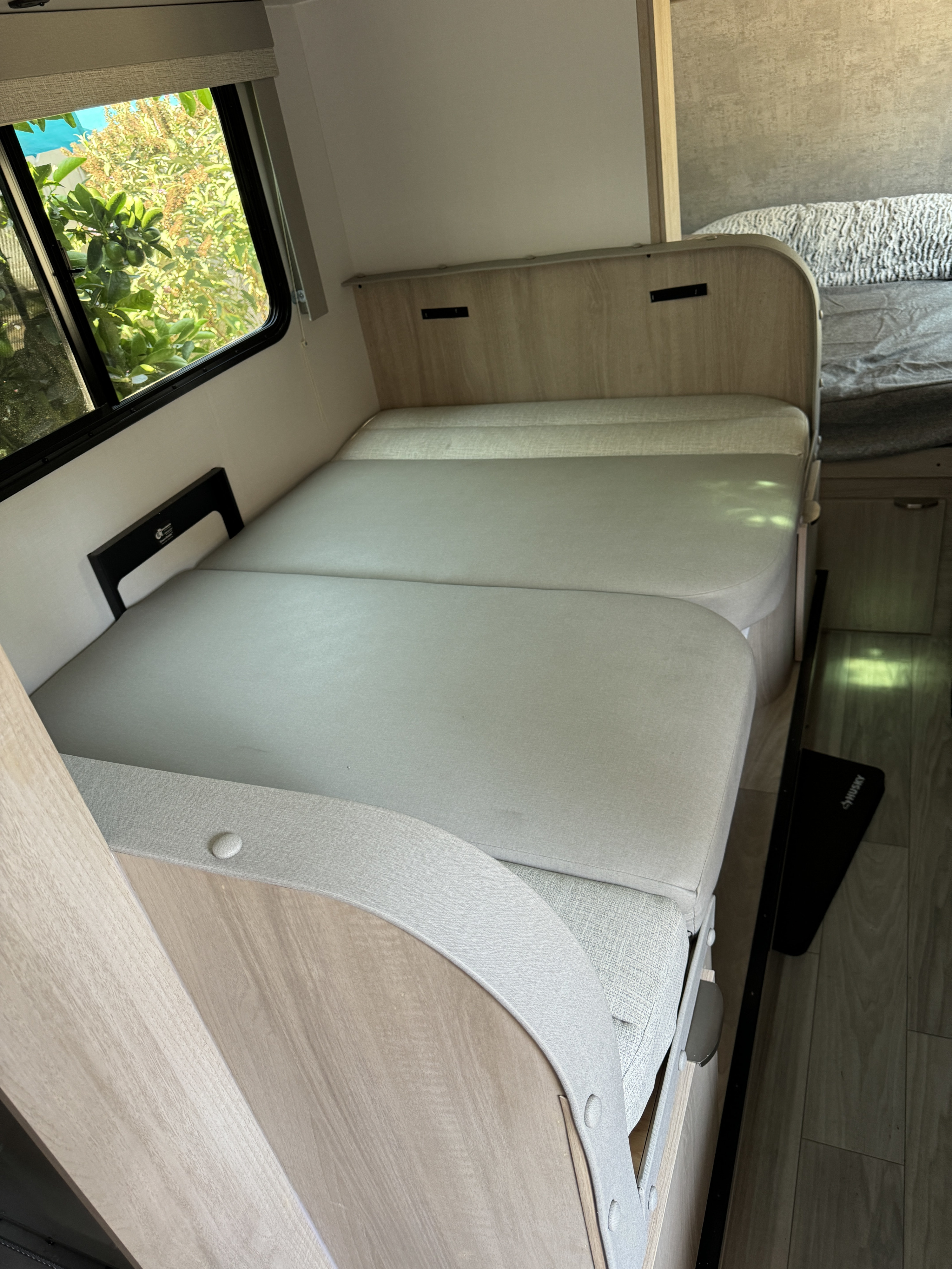 Spacious RV rental interior features a convertible light gray cushioned bed next to a large window.. Winnebago Micro Mini 2023