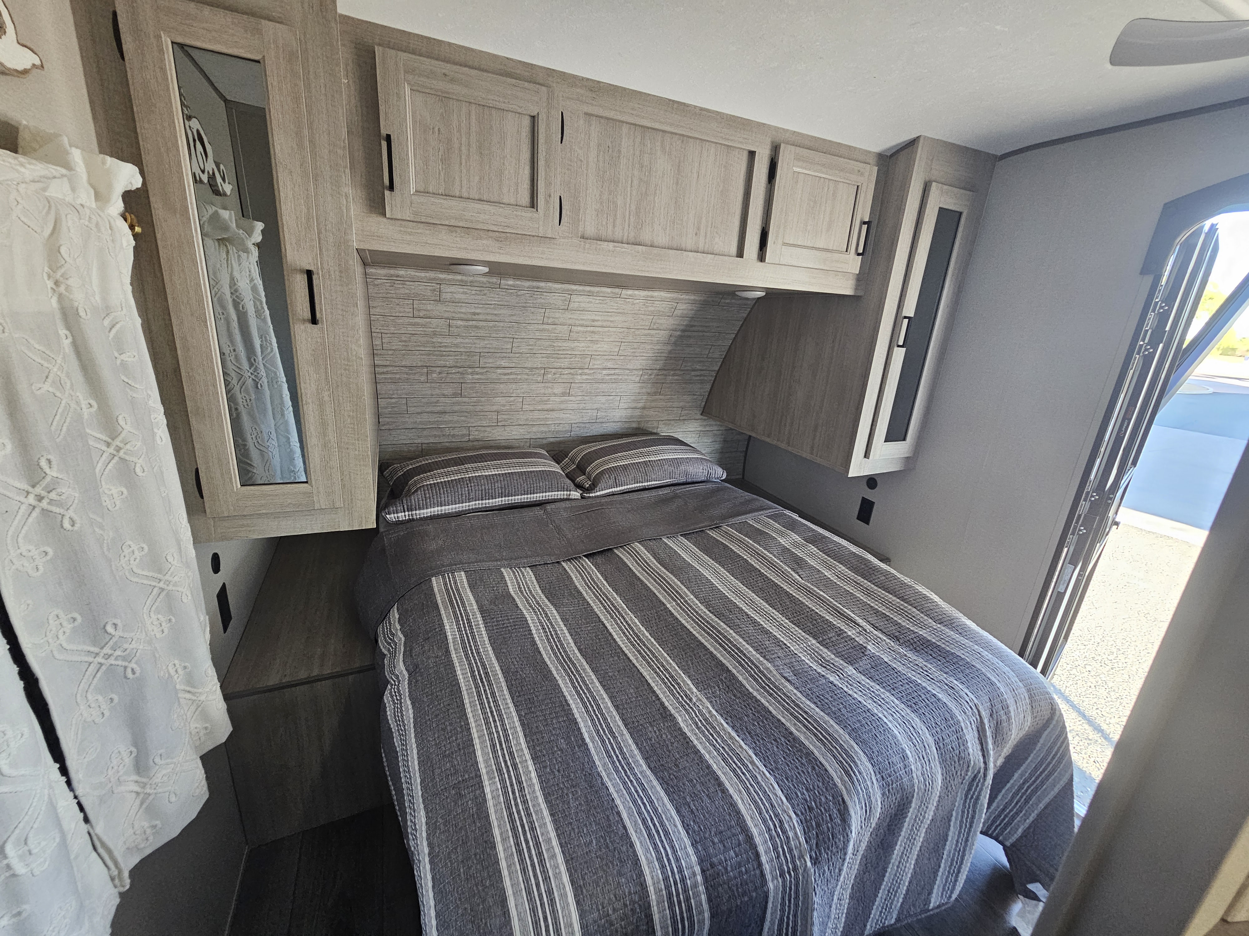 Cozy RV rental bedroom featuring a comfortable bed with striped bedding, built-in cabinets, and a side mirror.. Coachmen Catalina 2024