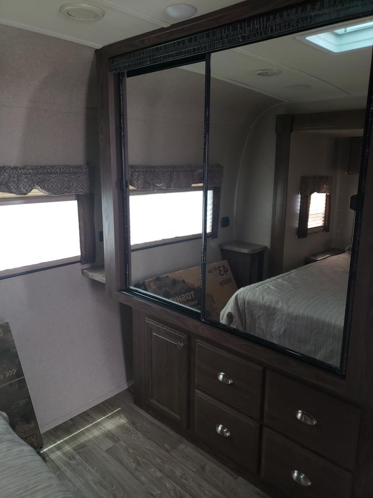 Inside an RV rental: a bedroom with dark wood mirrored closet, dresser drawers, and windows. Compact, functional design.. Forest River Flagstaff Classic 2019
