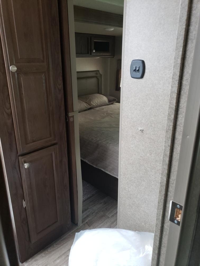 RV rental interior: From a hallway, a bedroom with a bed is visible, with a dark wood storage cabinet on the left.. Forest River Flagstaff Classic 2019