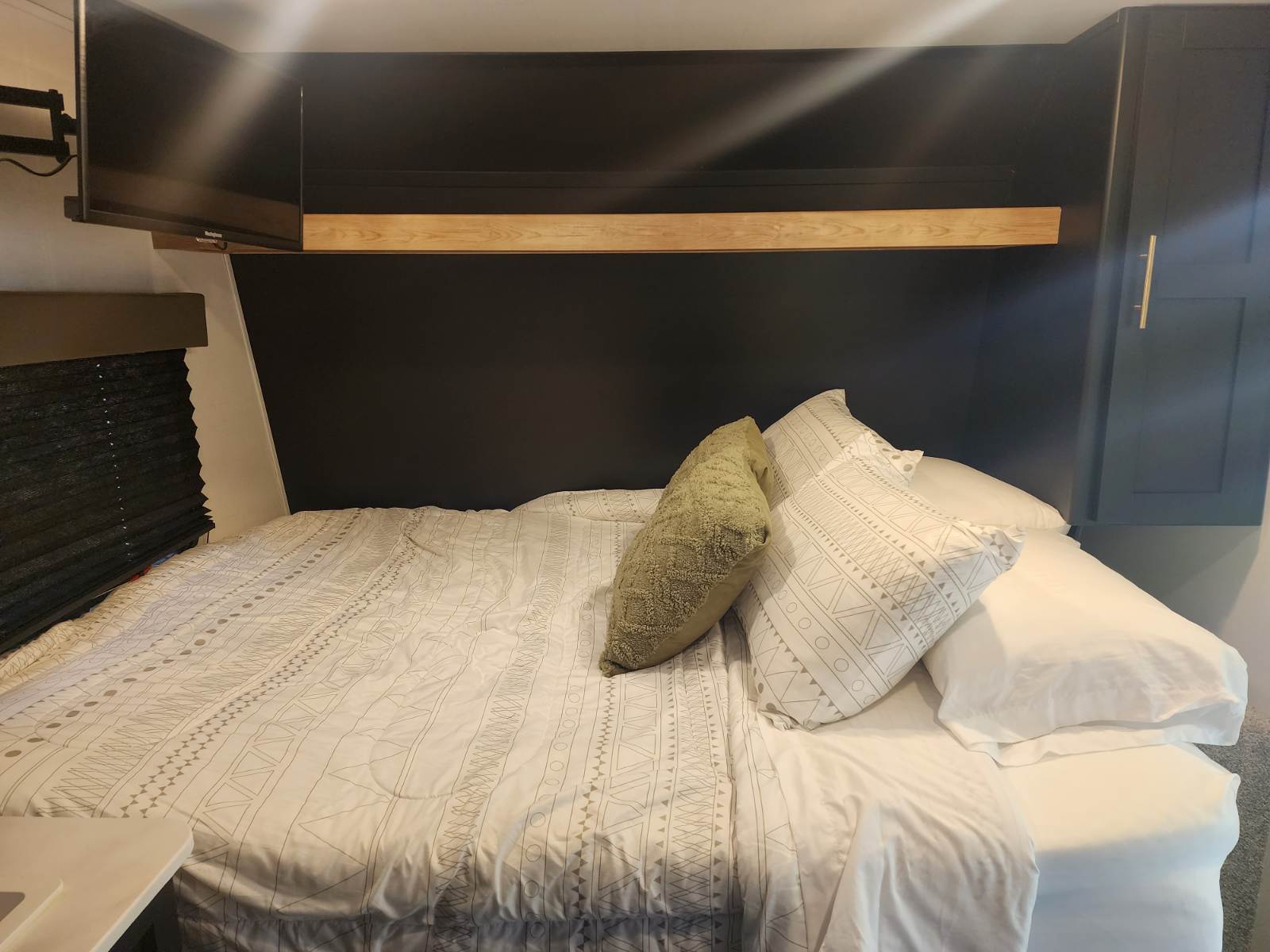 Spacious RV rental bedroom with modern dark decor, comfortable bed, TV, and pleated blinds.. Keystone RV Springdale 2022