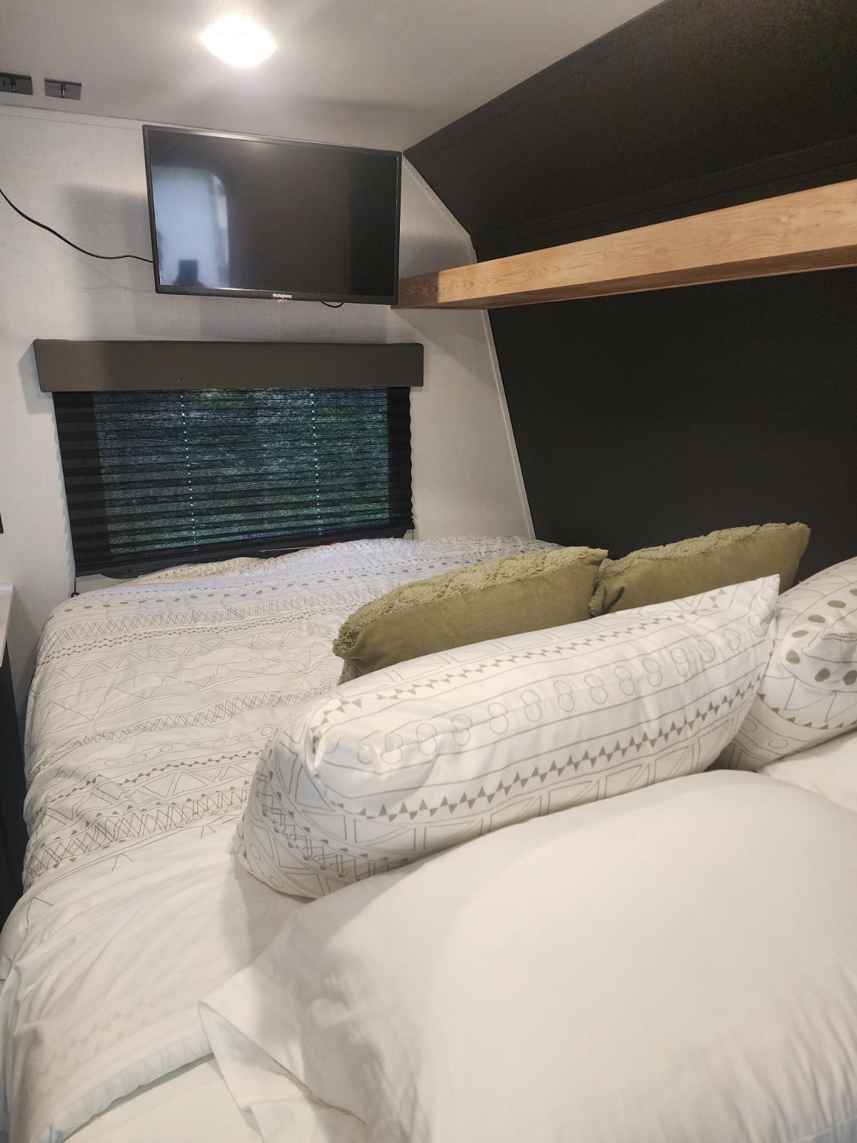 An inviting RV rental bedroom featuring a bed with patterned linens, green pillows, wall-mounted TV, window, and wooden beam.. Keystone RV Springdale 2022