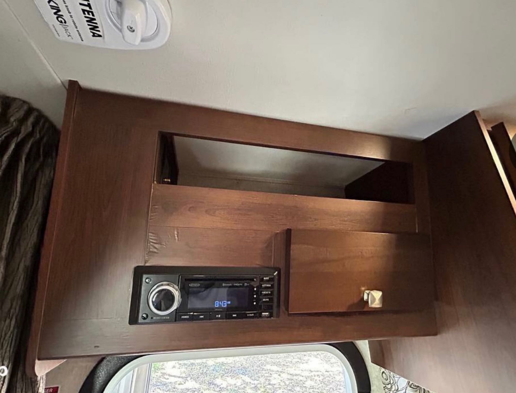 RV rental interior: a dark wood overhead cabinet with an integrated media player and small storage door. KING JACK antenna visible.. Forest River Mercedes 2019