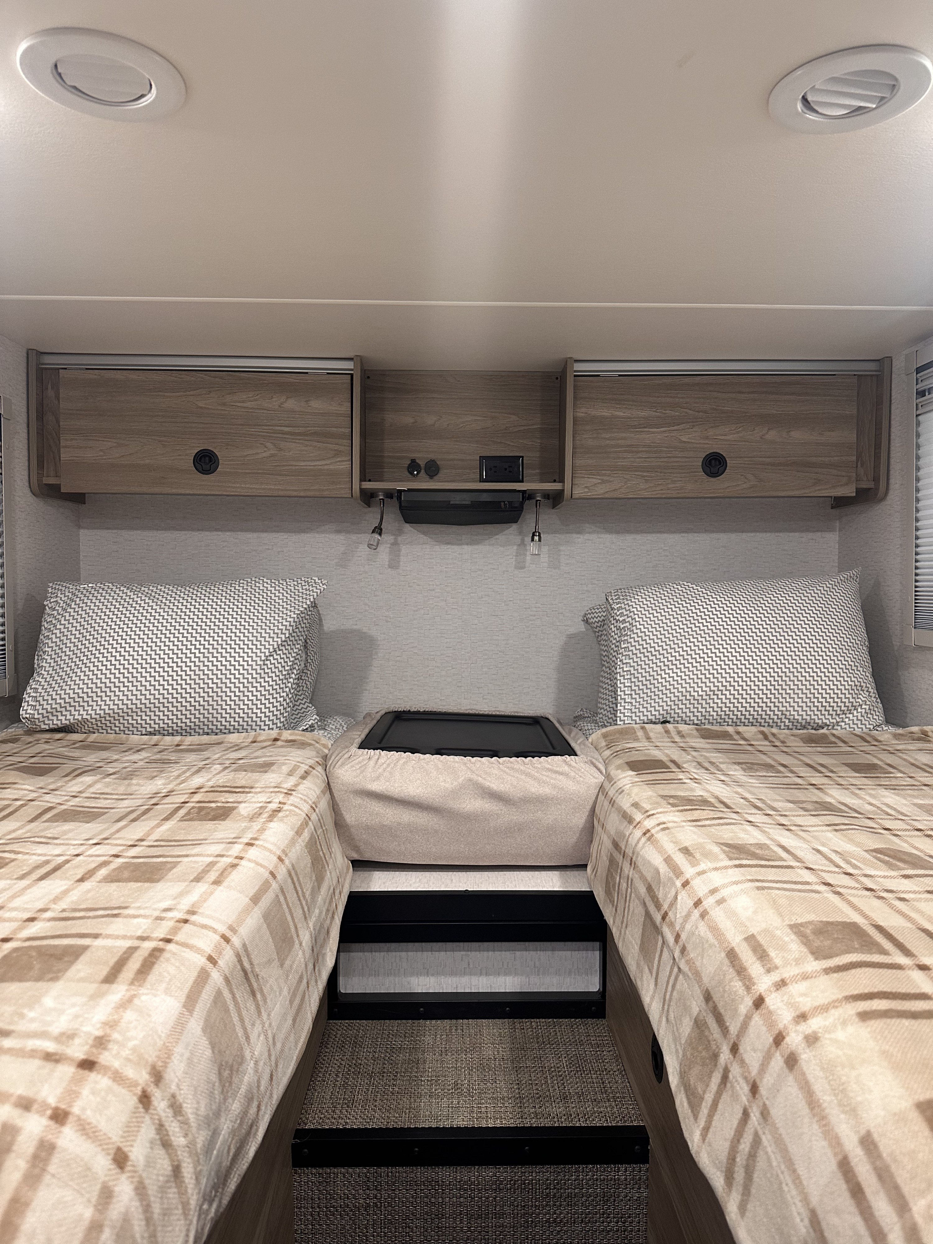 Cozy RV rental bedroom with twin beds, plaid blankets, overhead storage, and a central charging station.. Winnebago Ekko 2025