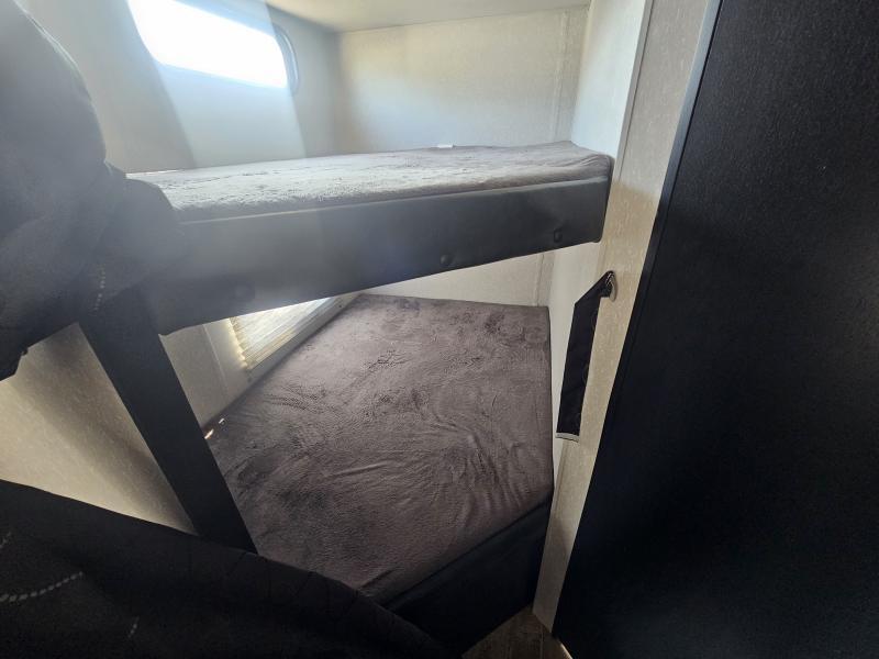 RV rental bunk beds: Two stacked beds with gray bedding inside a cozy RV interior, illuminated by a window.. Forest River Cherokee Grey Wolf 2022