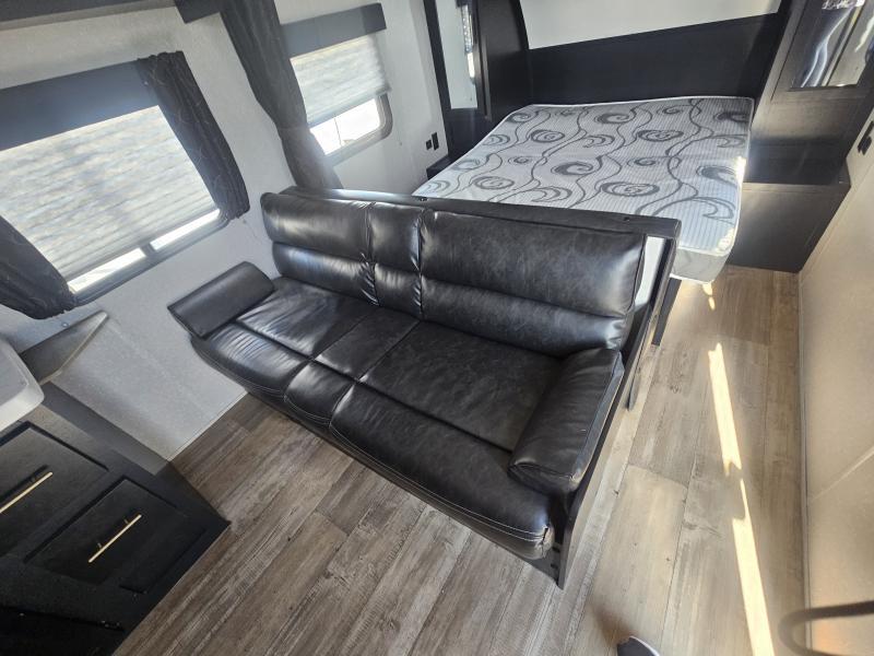 RV rental interior: compact living space with a black leather sofa, wood-look flooring, and a comfortable bed.. Forest River Cherokee Grey Wolf 2022