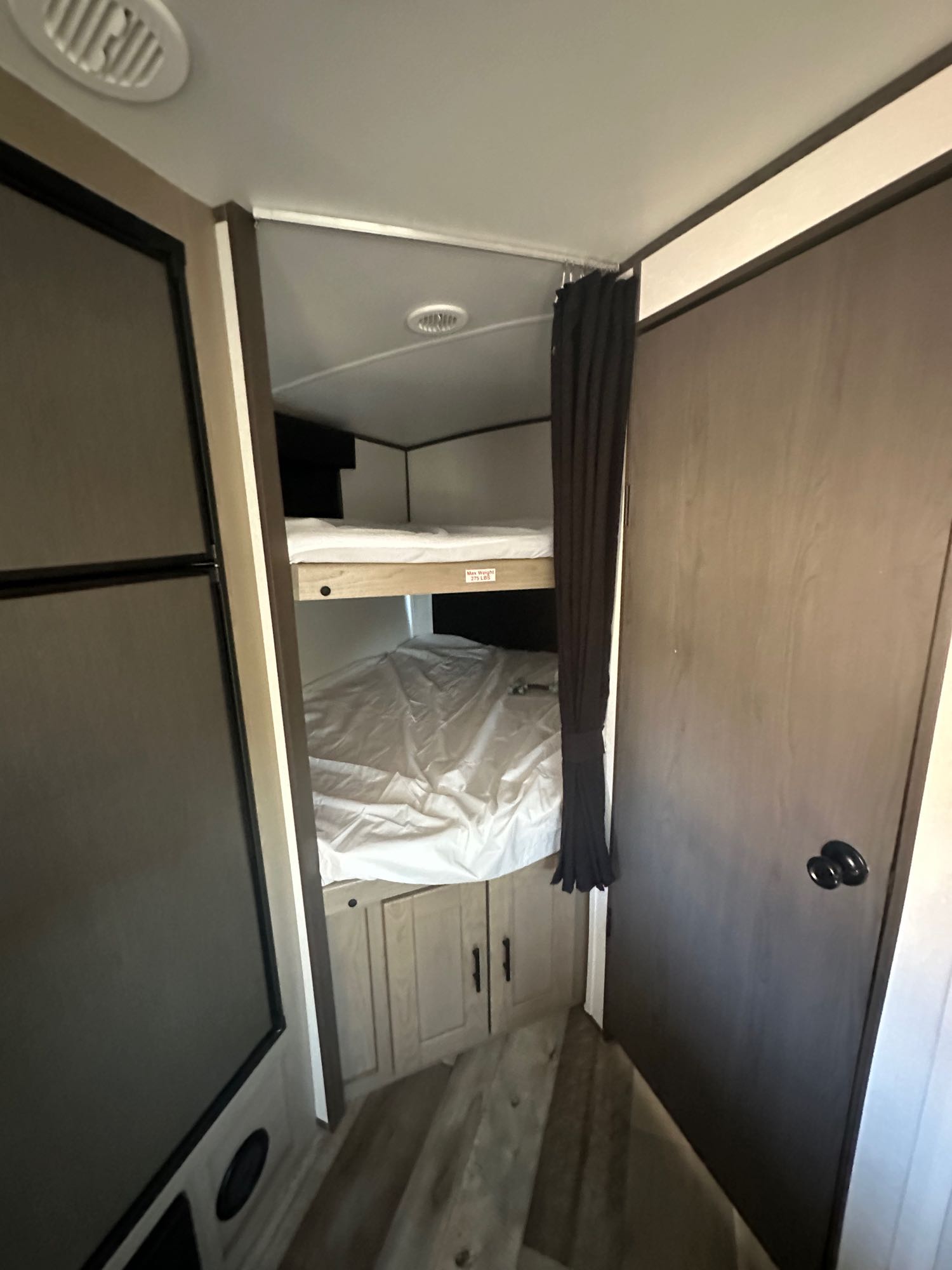 An rv rental interior showing two bunk beds, a privacy curtain, fridge, and under-bunk storage.. Heartland RVs Sundance Ultra Lite 2021