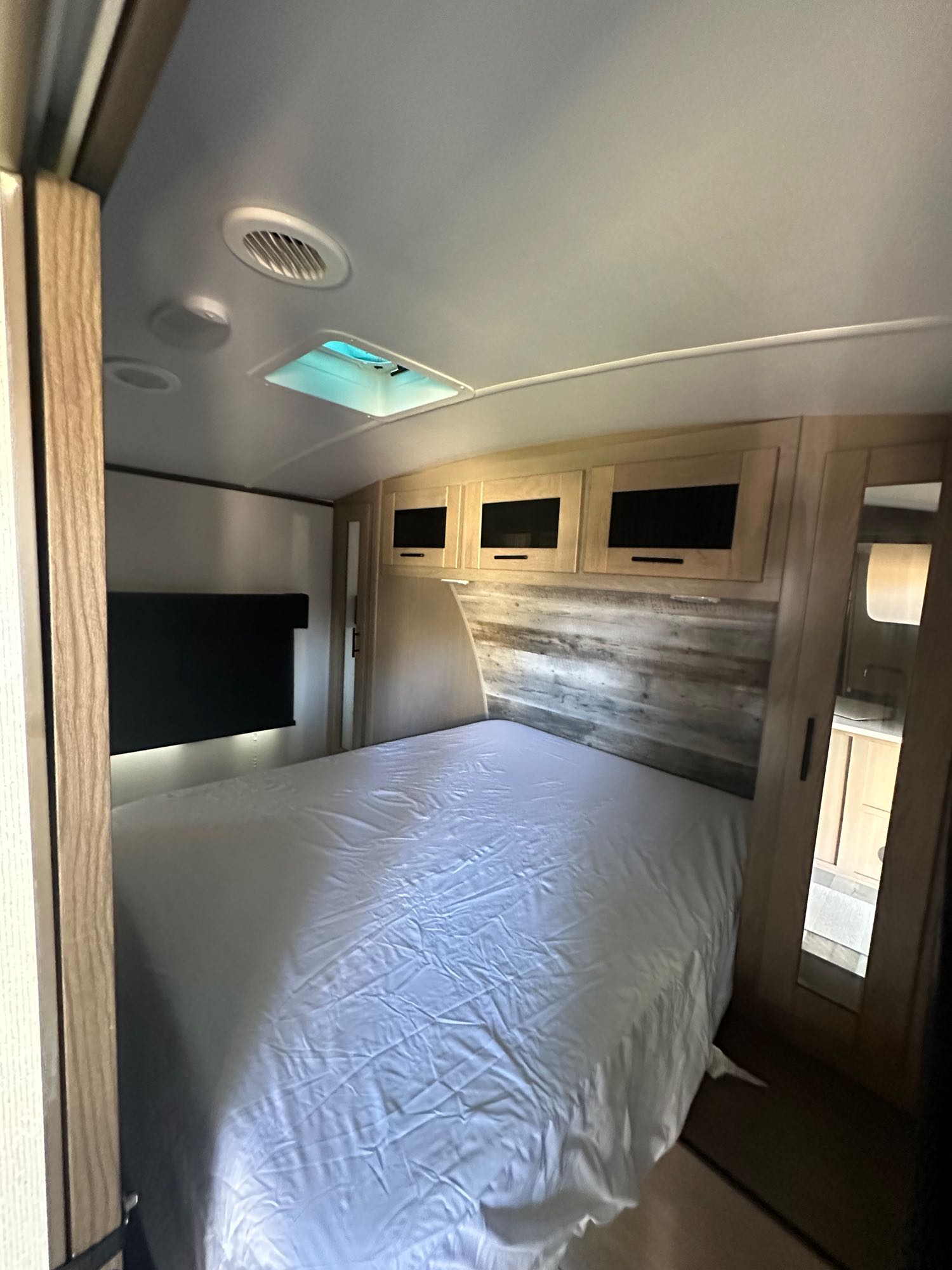 RV rental bedroom: a cozy space with a neatly made bed, wooden headboard, cabinets, ceiling vent, and mirror.. Heartland RVs Sundance Ultra Lite 2021